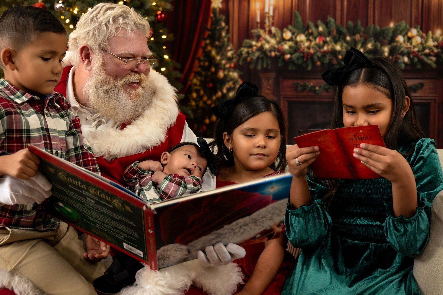 Santa Claus reads a Christmas book with four young children by a decorated fireplace during a festive holiday photo session.