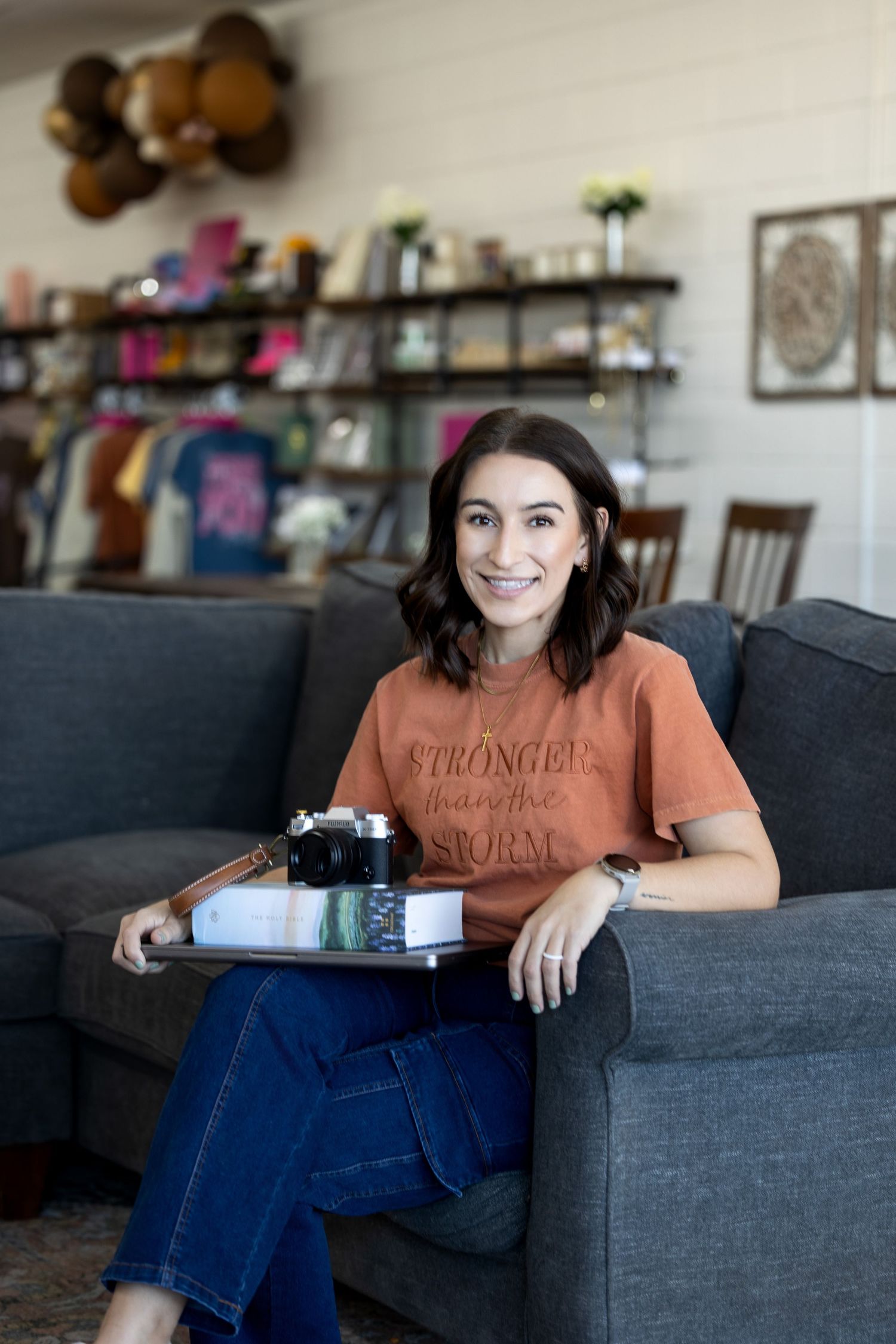 A woman in a brown shirt and jeans relaxes on a gray couch in a modern living room setting.