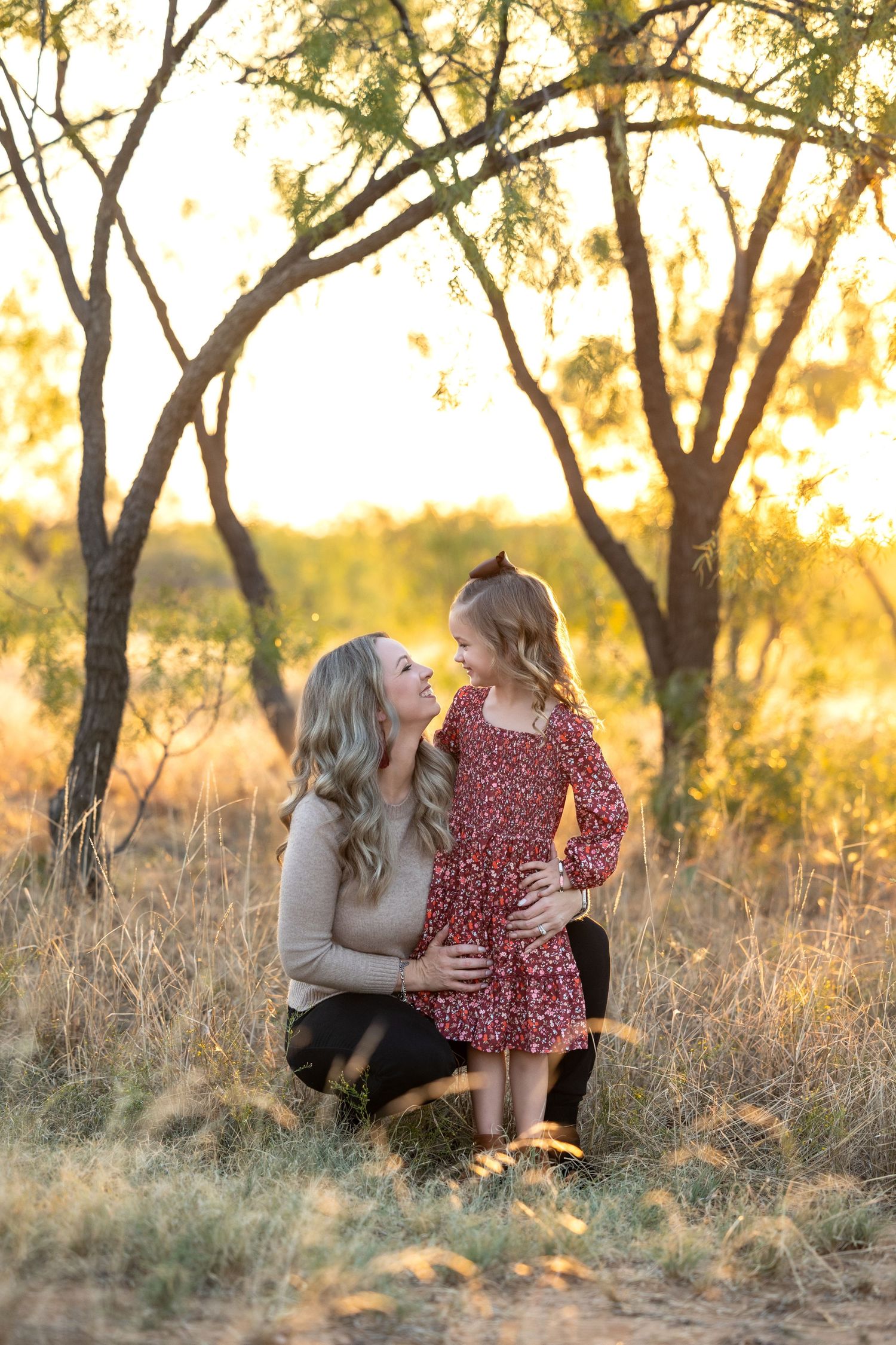 A couple shares intimate moments in a sun-drenched field with golden grass and trees during sunset.