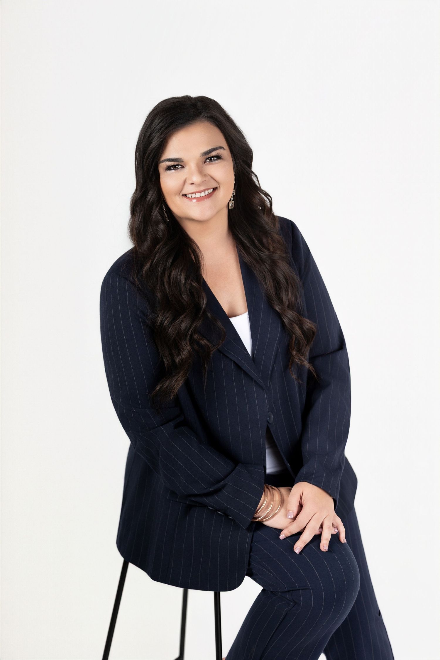 Professional studio portrait of someone wearing a navy pinstriped blazer posing with a chair against white background.
