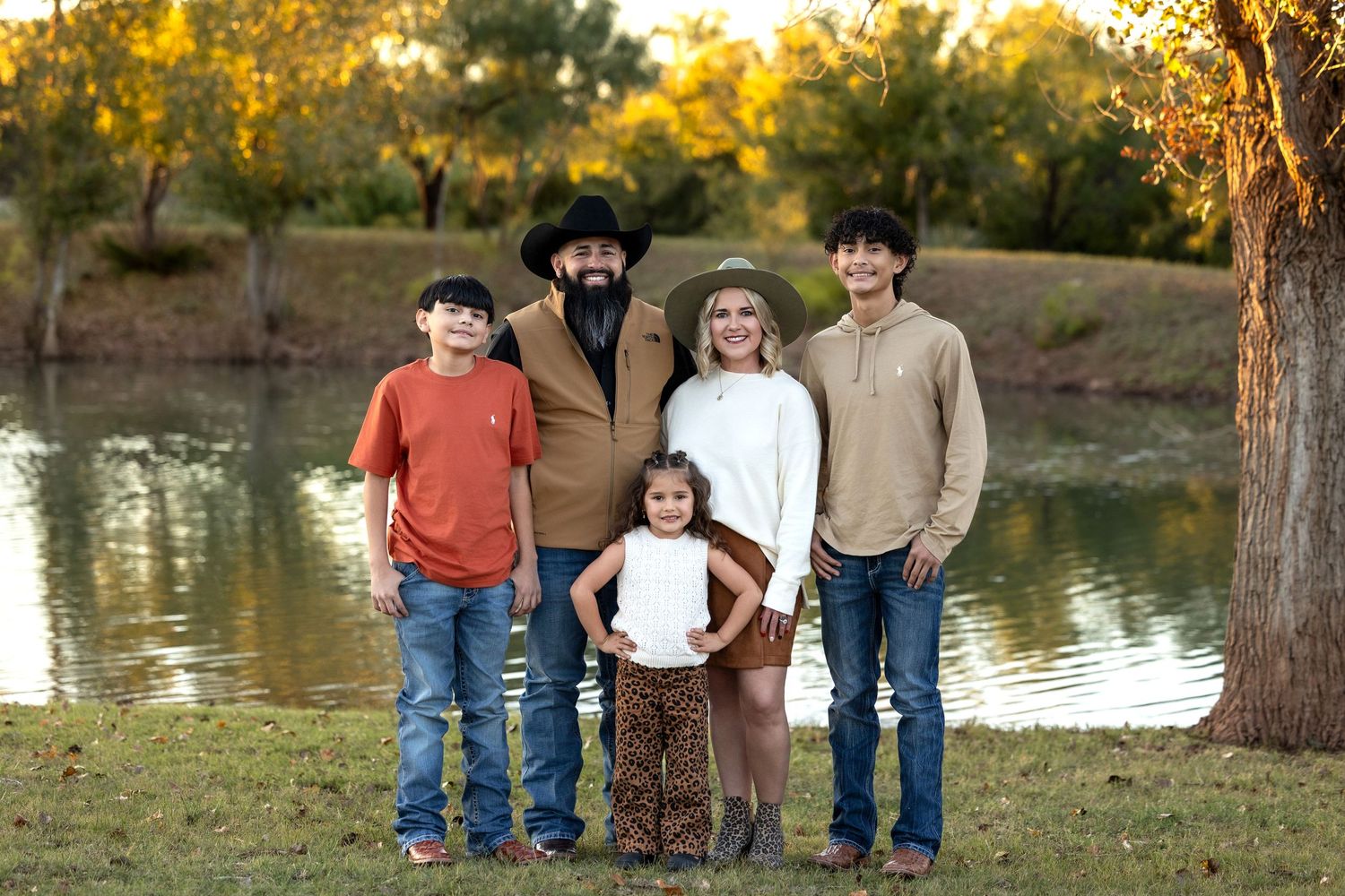 A group of people stand near a tranquil lake at sunset during an autumn photo session.