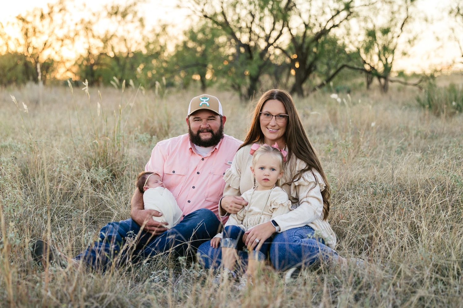 A family sits together in a sunlit field of tall grass during golden hour.