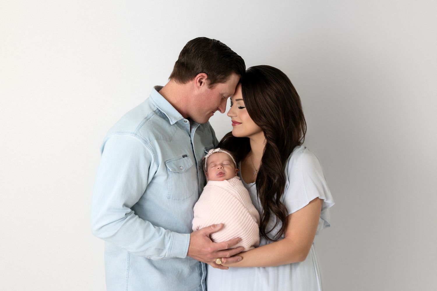 A series of tender family moments showing parents holding and kissing their newborn baby in a light-filled studio setting.