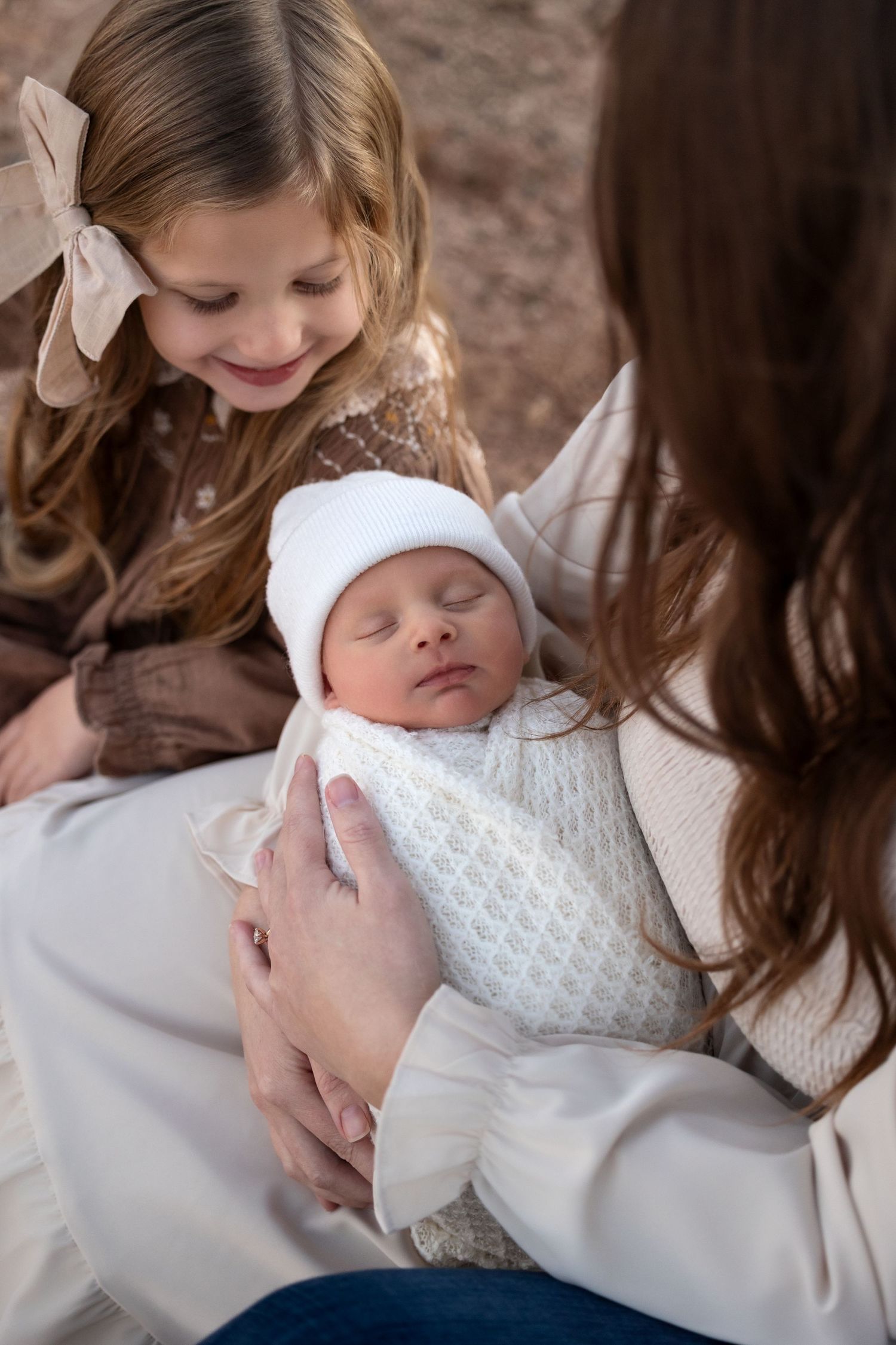 A sleeping newborn baby in white clothing is cradled lovingly while being admired by family members.