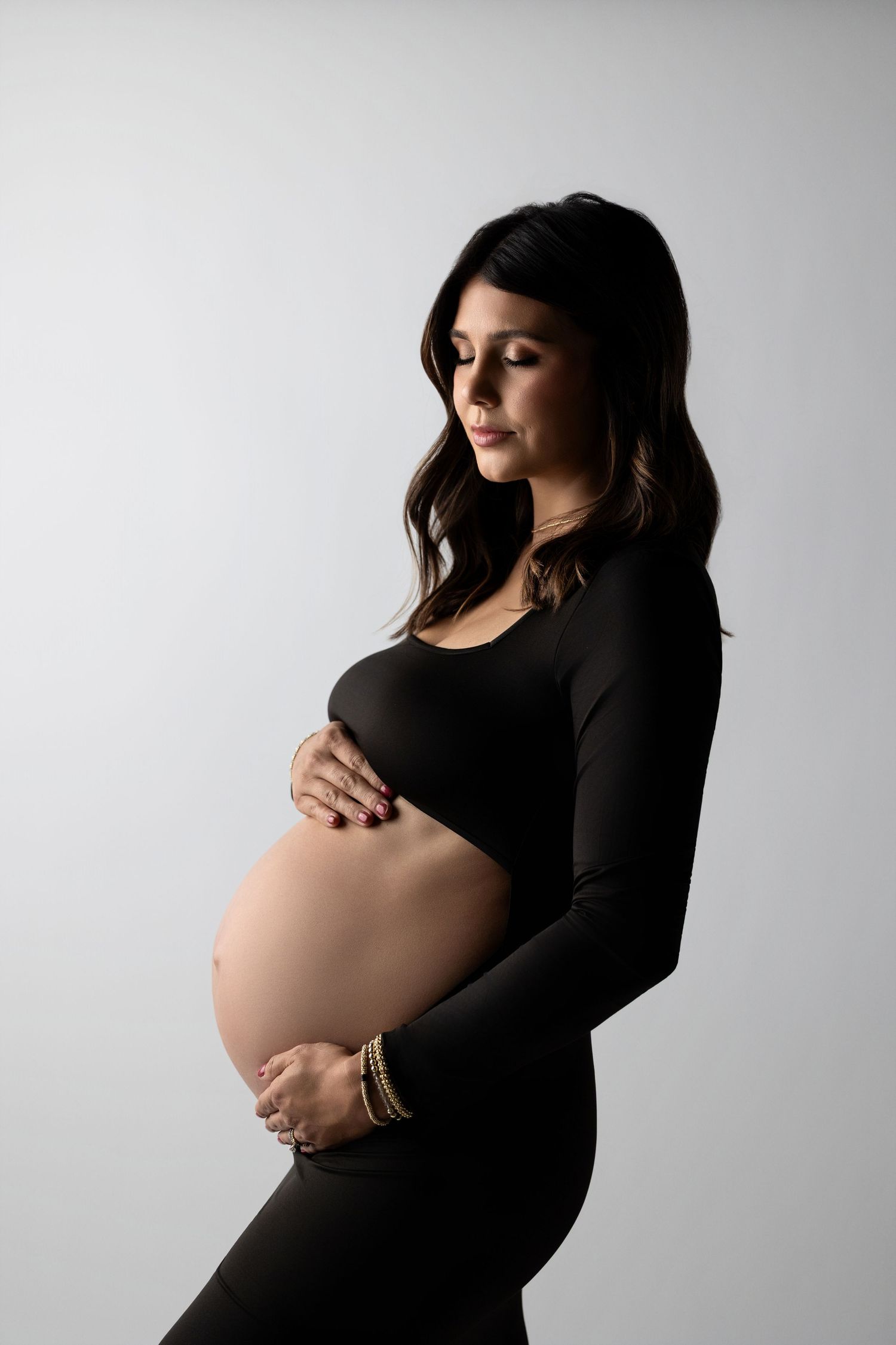 Side view of an elegant maternity portrait showing a pregnant figure in black against a light background.