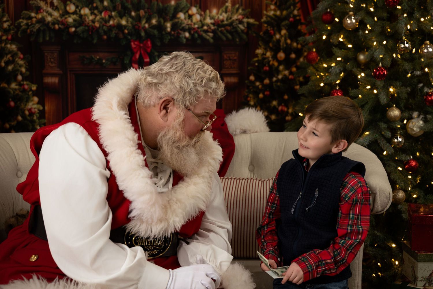 A boy sits with Santa Claus near a decorated Christmas tree, sharing a magical holiday moment.
