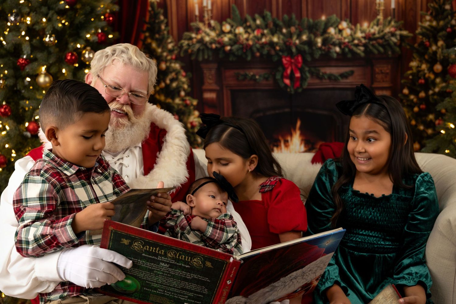 Santa Claus reads a festive book with four happy children near a decorated Christmas tree and fireplace.