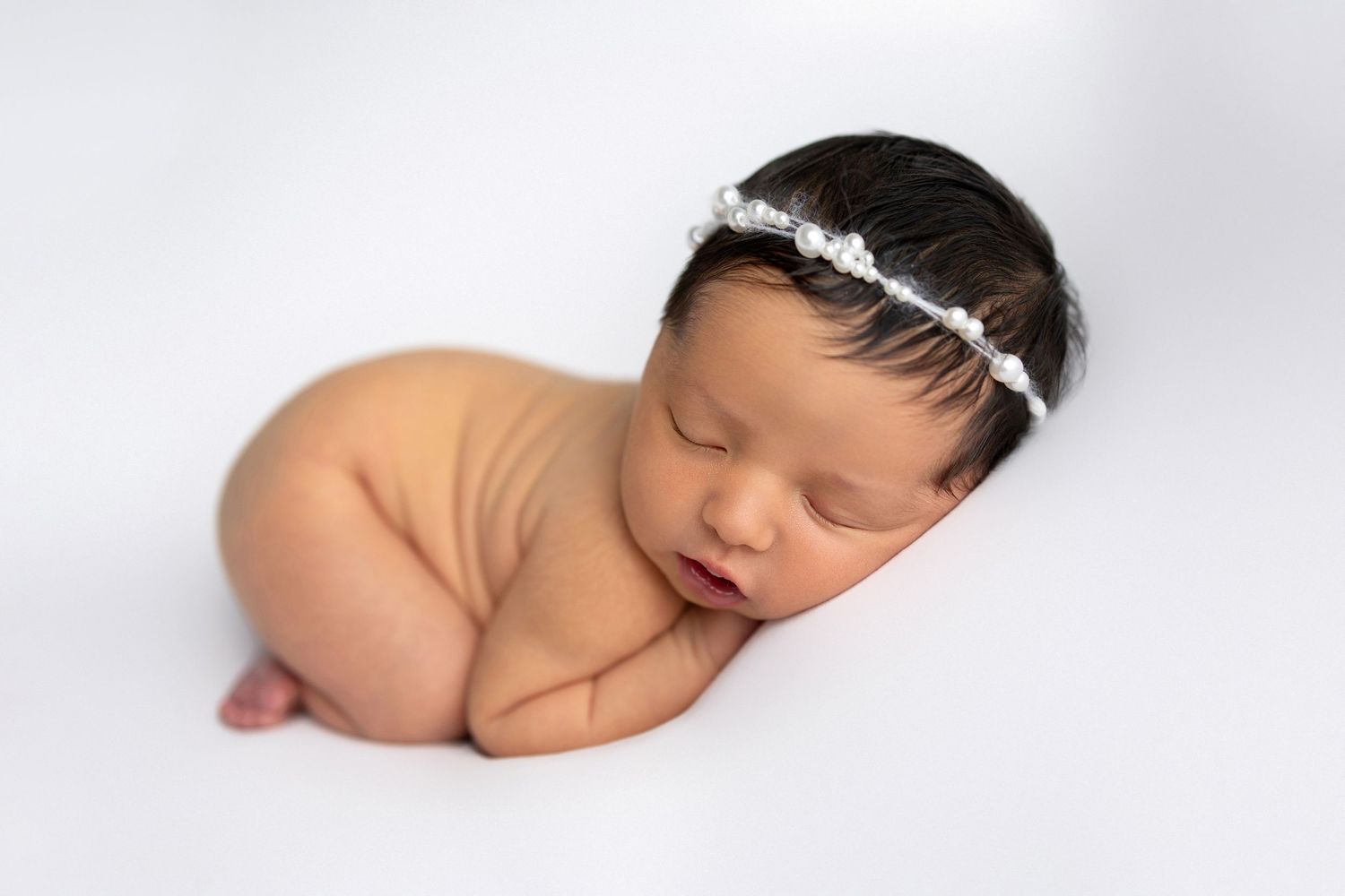 A sleeping newborn baby wearing a delicate silver headband rests peacefully in a minimalist photo collage.