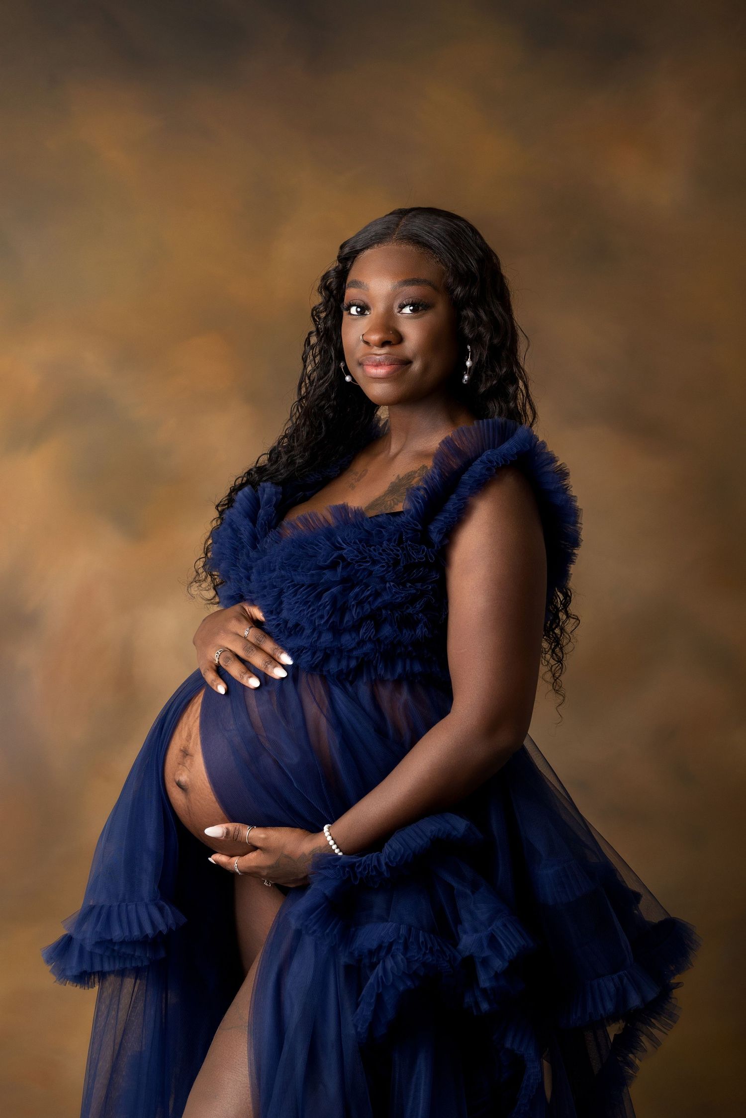 Luxury maternity portrait in ruffled navy blue gown against warm brown backdrop in Lubbock, Texas.