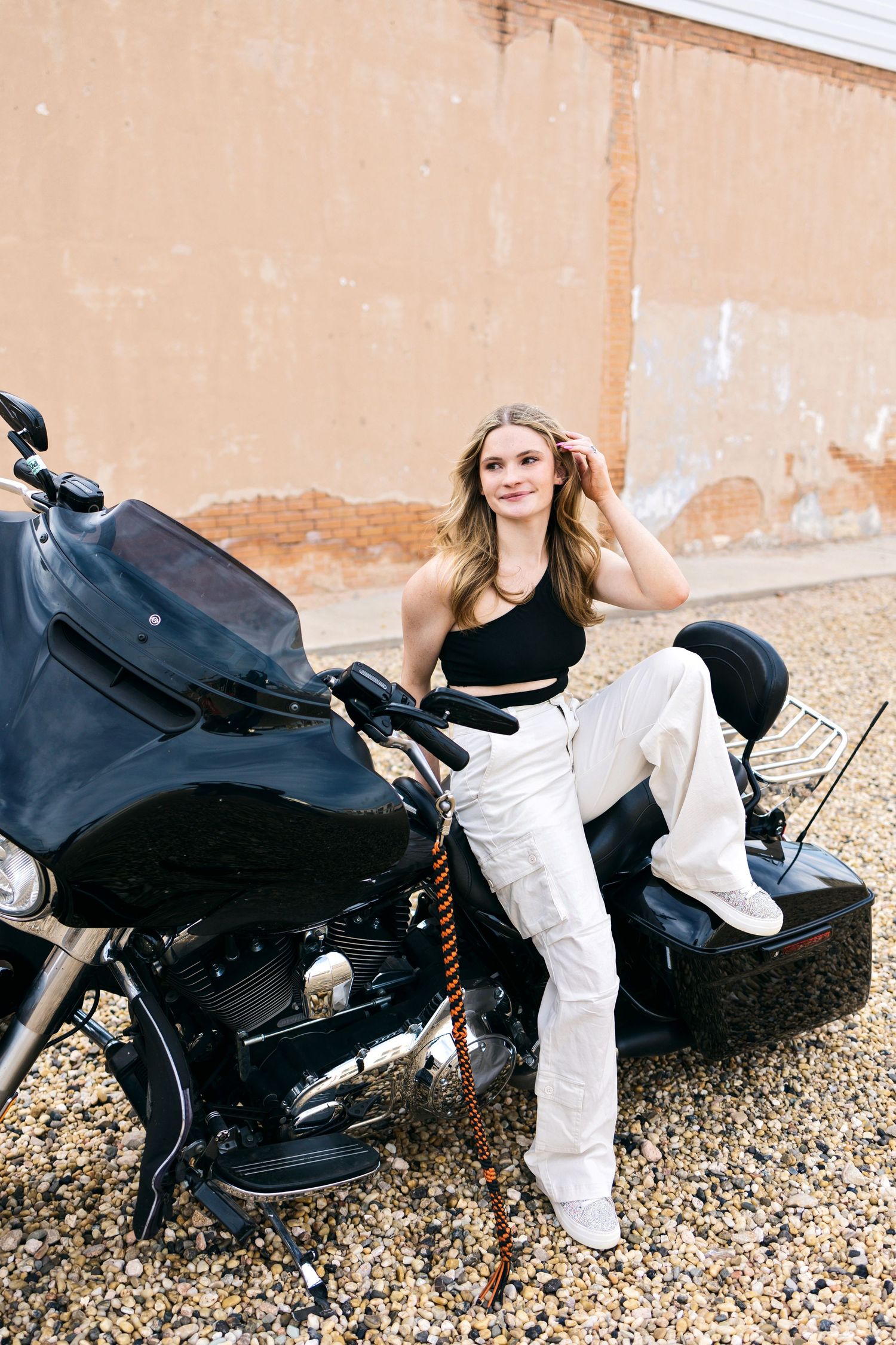 A sequence of photos showing someone in white pants posing with a black motorcycle on a gravel surface.
