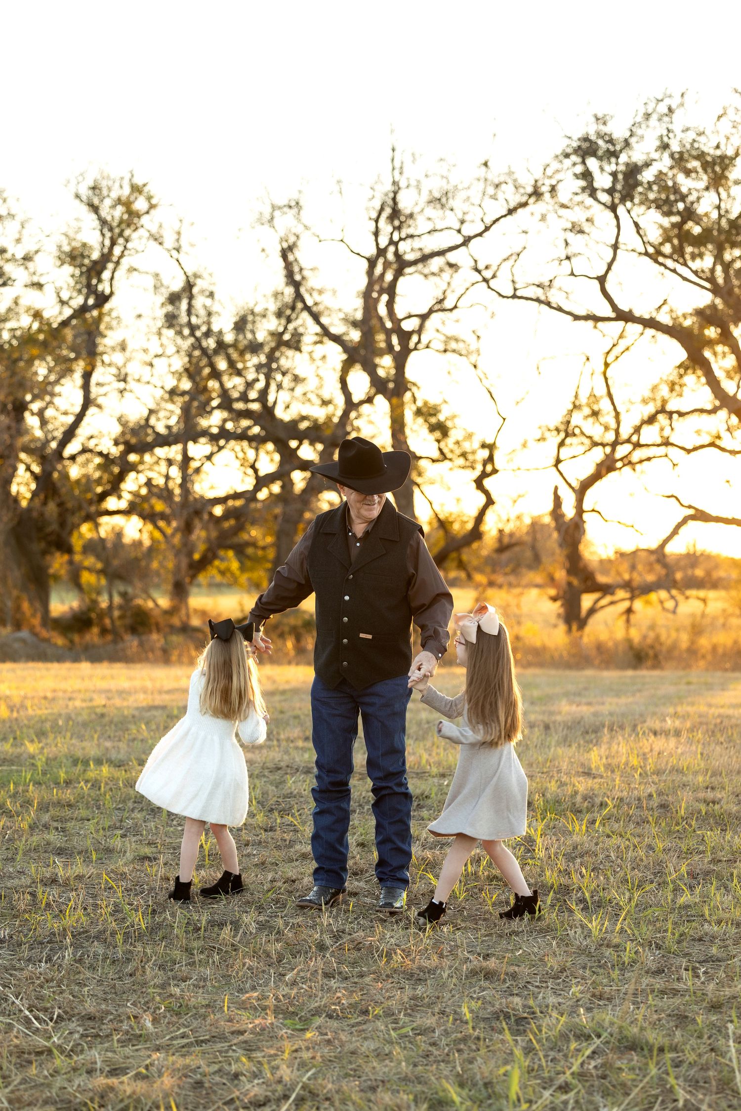 Family wearing rustic western outfits walking through a golden field at sunset with trees in background.