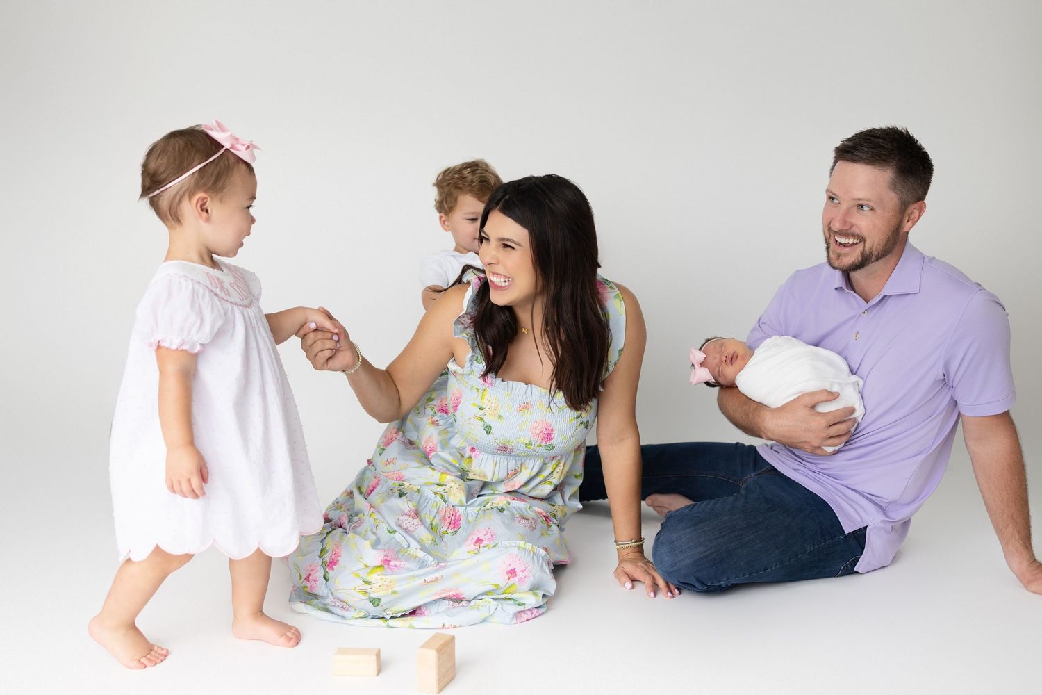 Family wearing white and purple clothing lying together on white floor during indoor photo session.