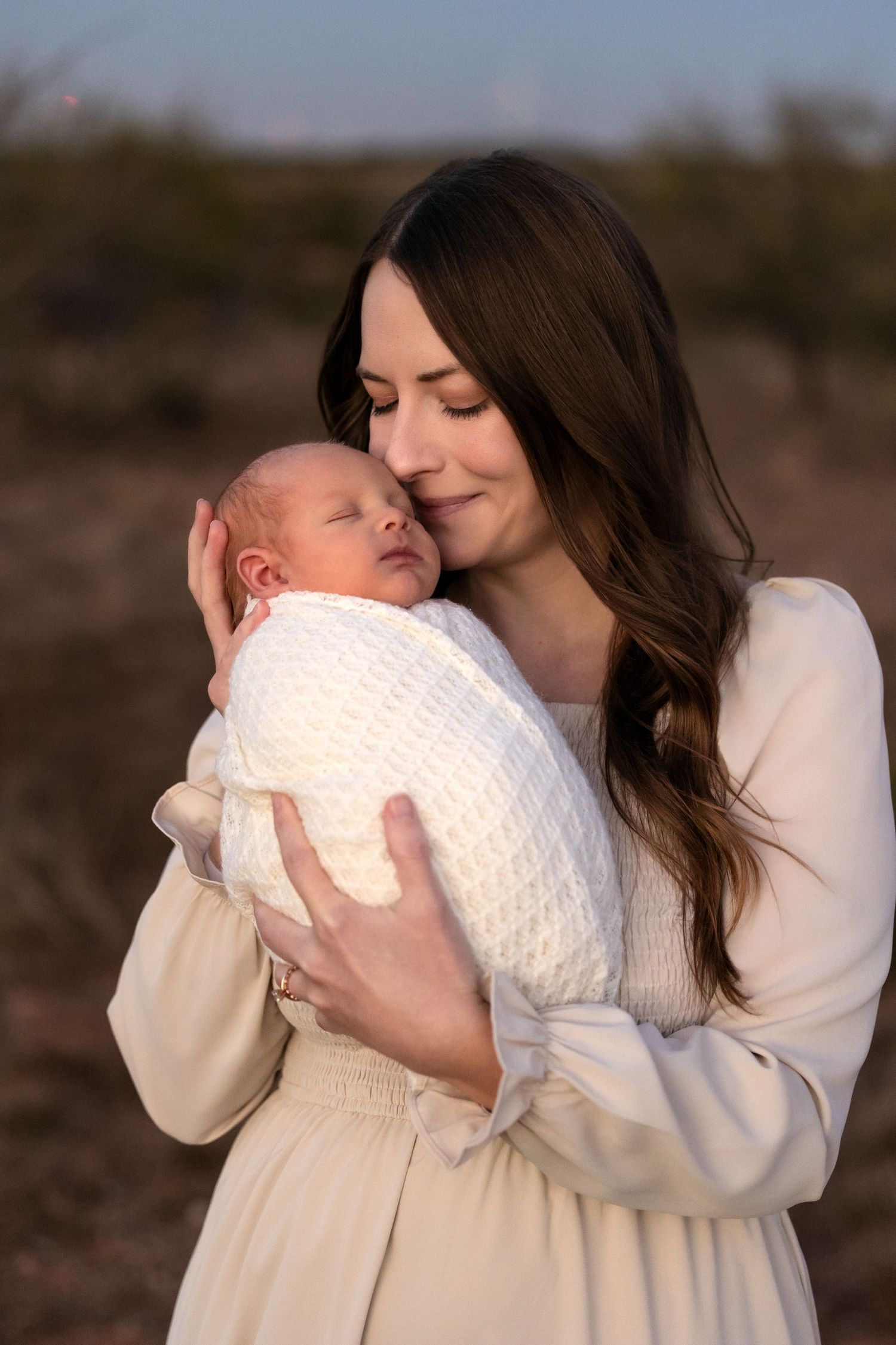 A tender moment between parent and newborn baby captured in soft natural lighting against a blurred outdoor background.