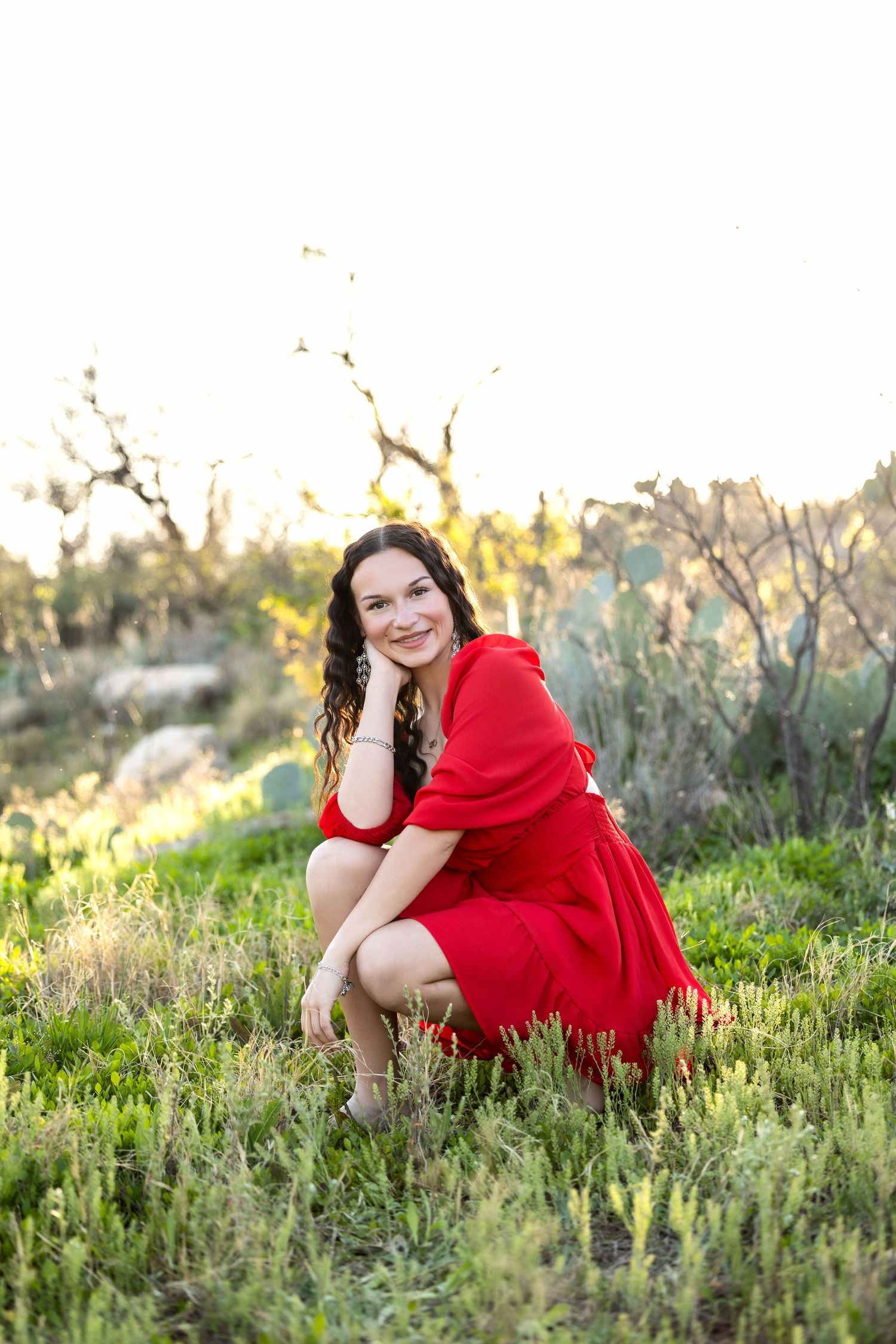 A person in a flowing red dress poses gracefully in a wildflower meadow during golden hour.