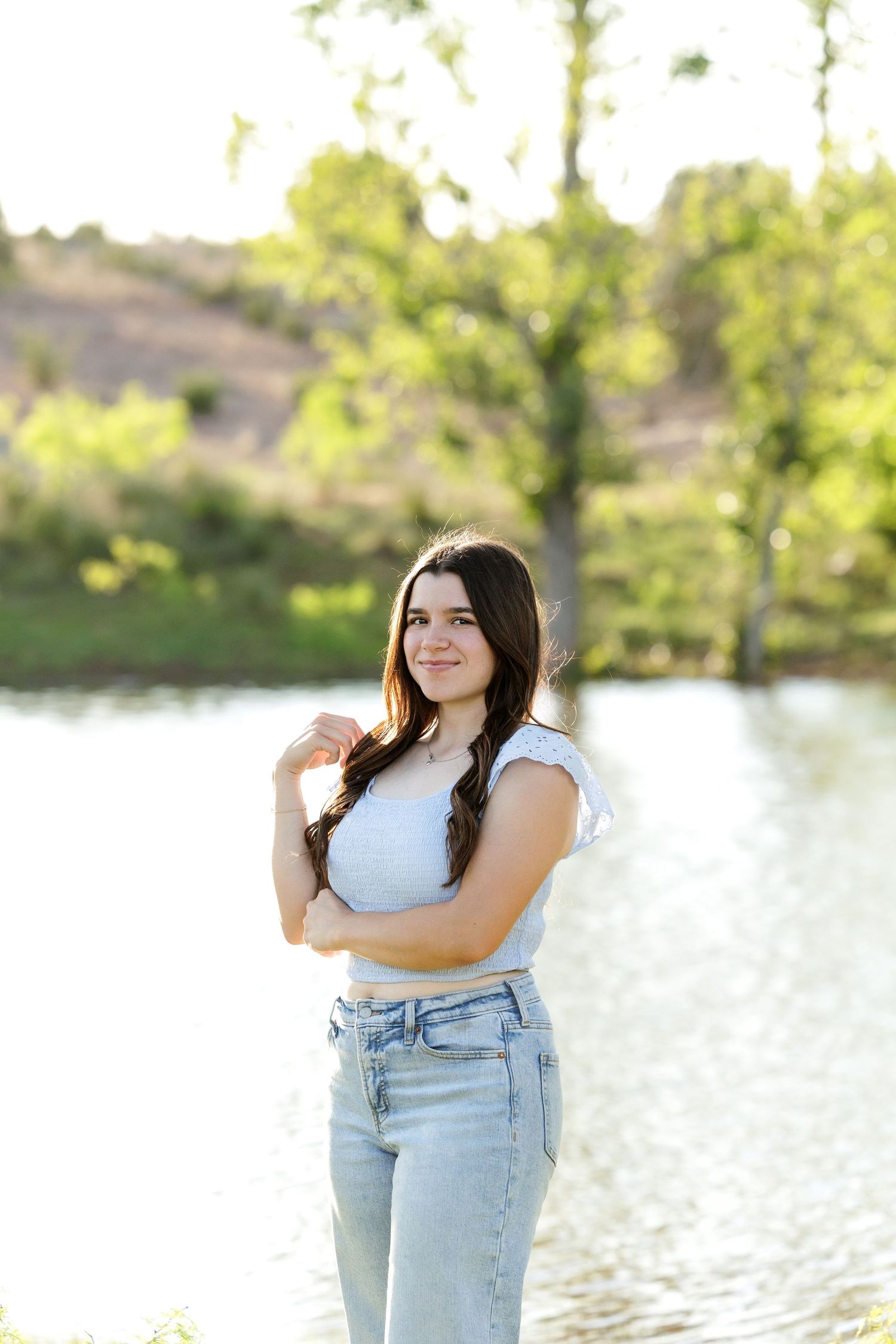 A casual outdoor photoshoot by a serene lake with light reflecting off the water in the background.