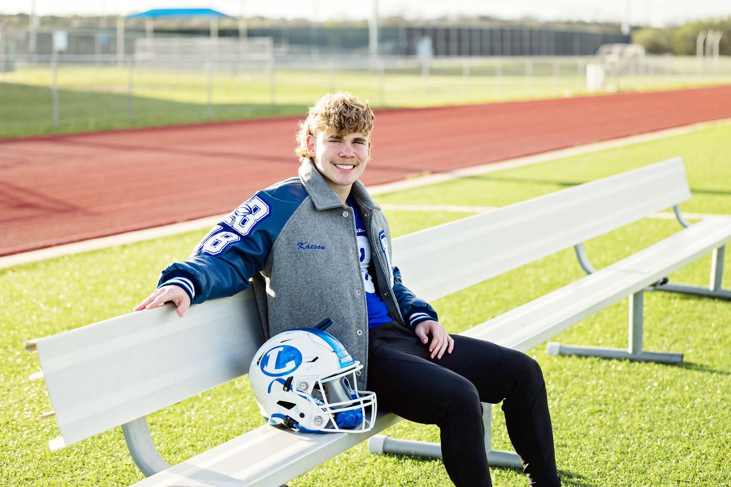 Student athlete sits on bleachers with laptop and football equipment during outdoor practice session.