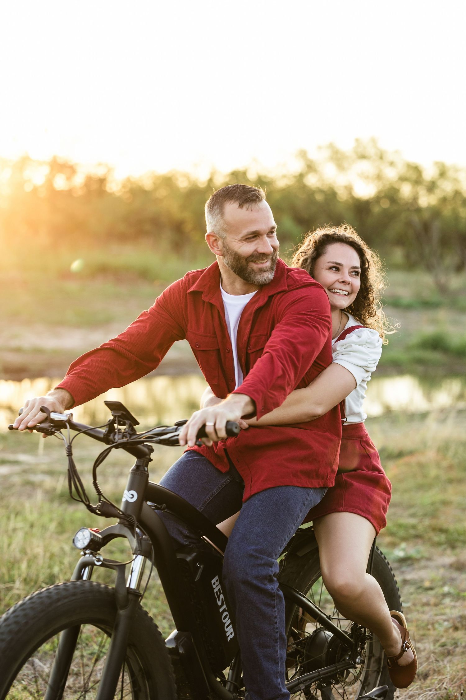 Couple sharing romantic moments on a motorcycle during golden hour sunset in a countryside setting.