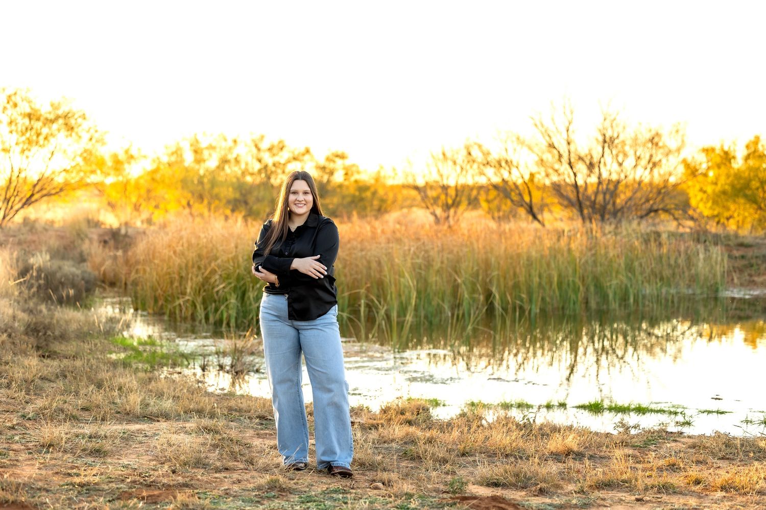 A couple embraces during a golden hour photoshoot in a sunlit field with tall grass and autumn colors.