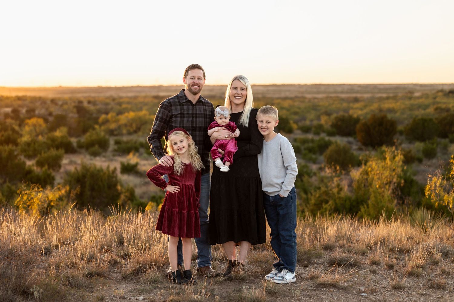 A family poses together at sunset in a desert landscape with brush and golden light.