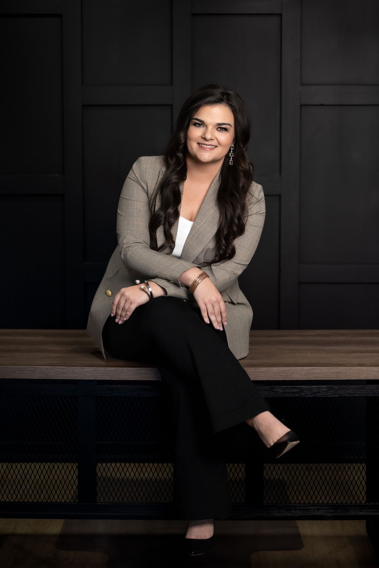 Professional studio portrait of someone in business attire sitting on a dark bench against a black background.