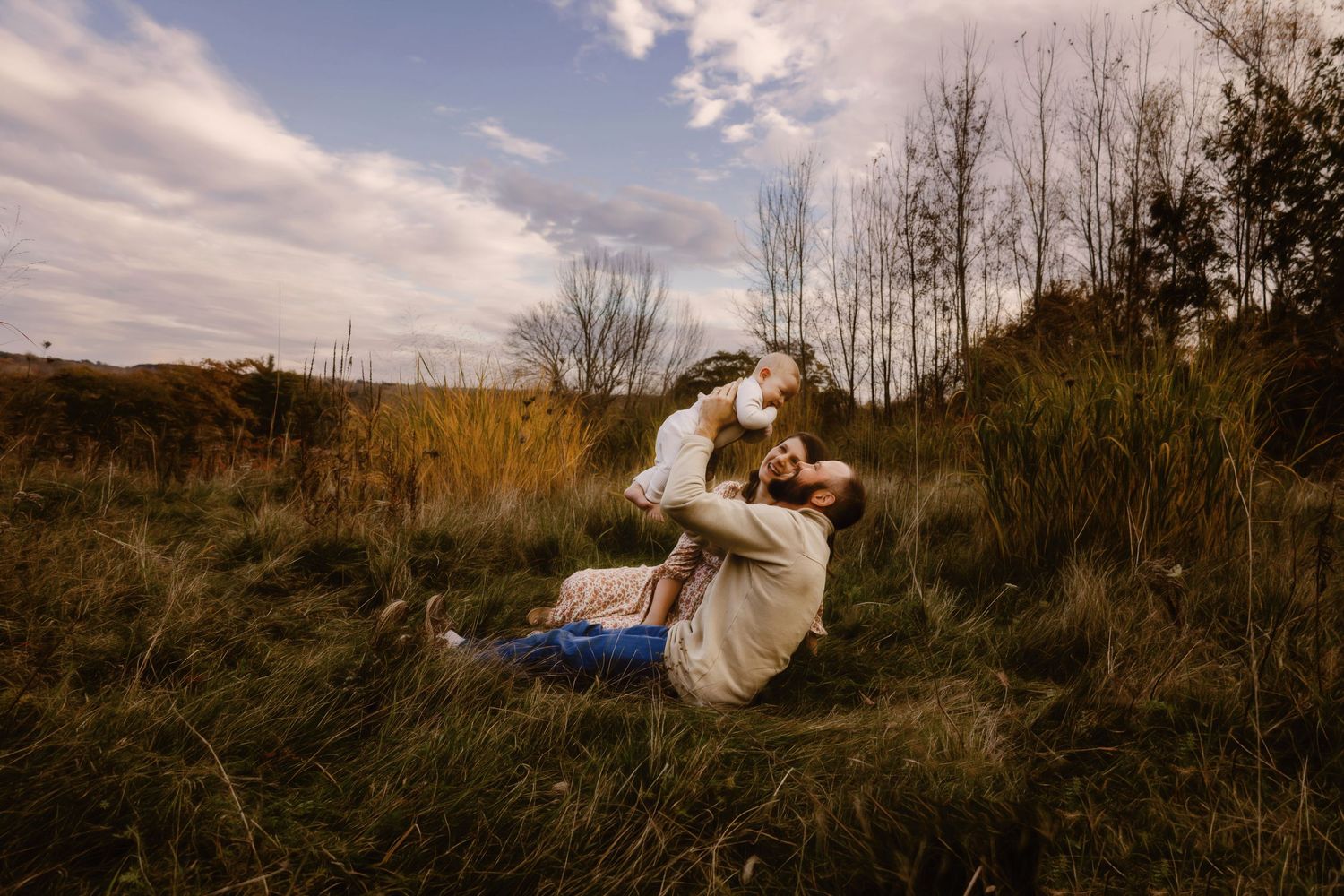 Intimate outdoor portrait in golden field with autumn trees in background.