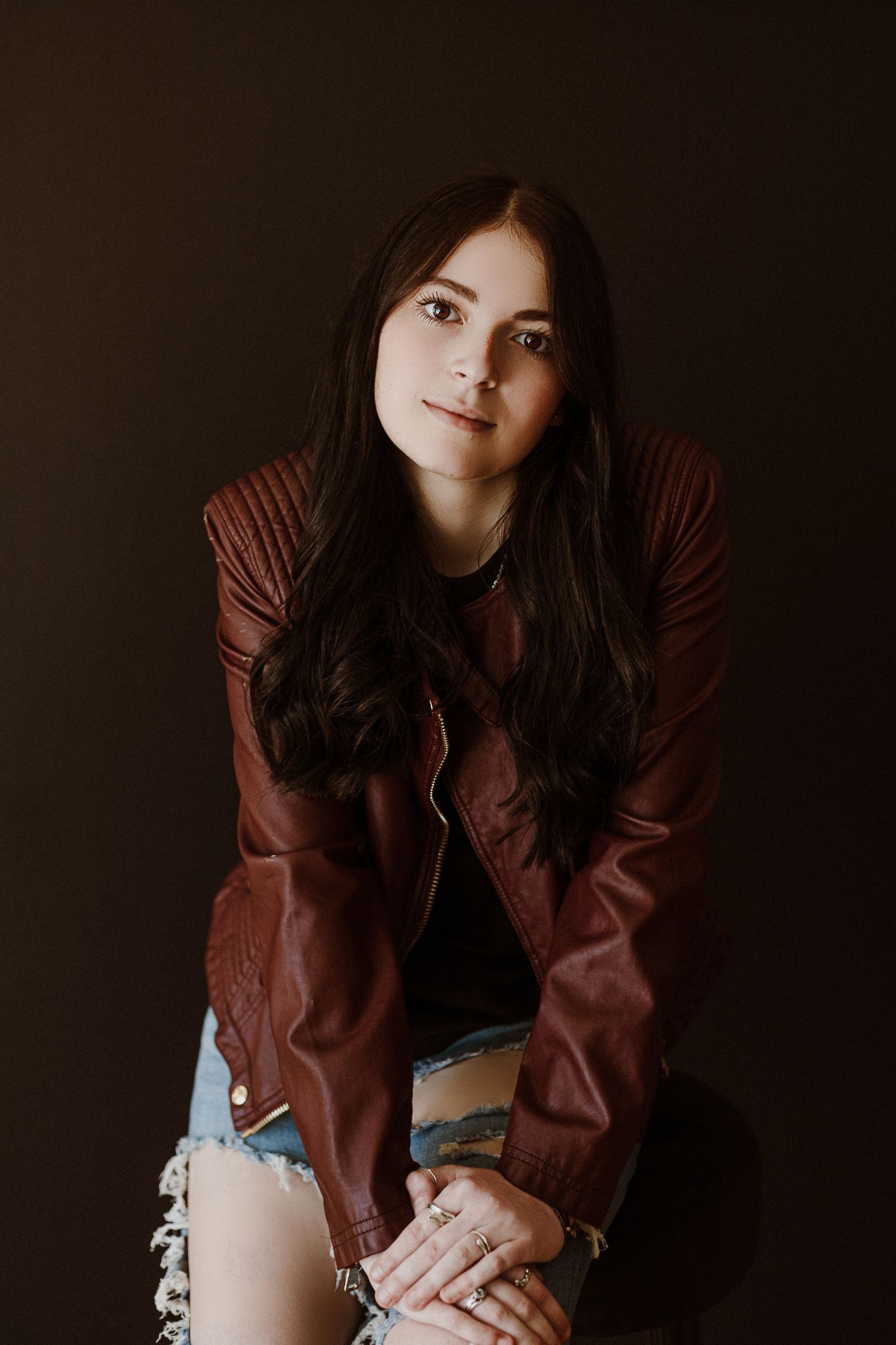 Studio portrait of a woman in a brown leather jacket against a dark background.