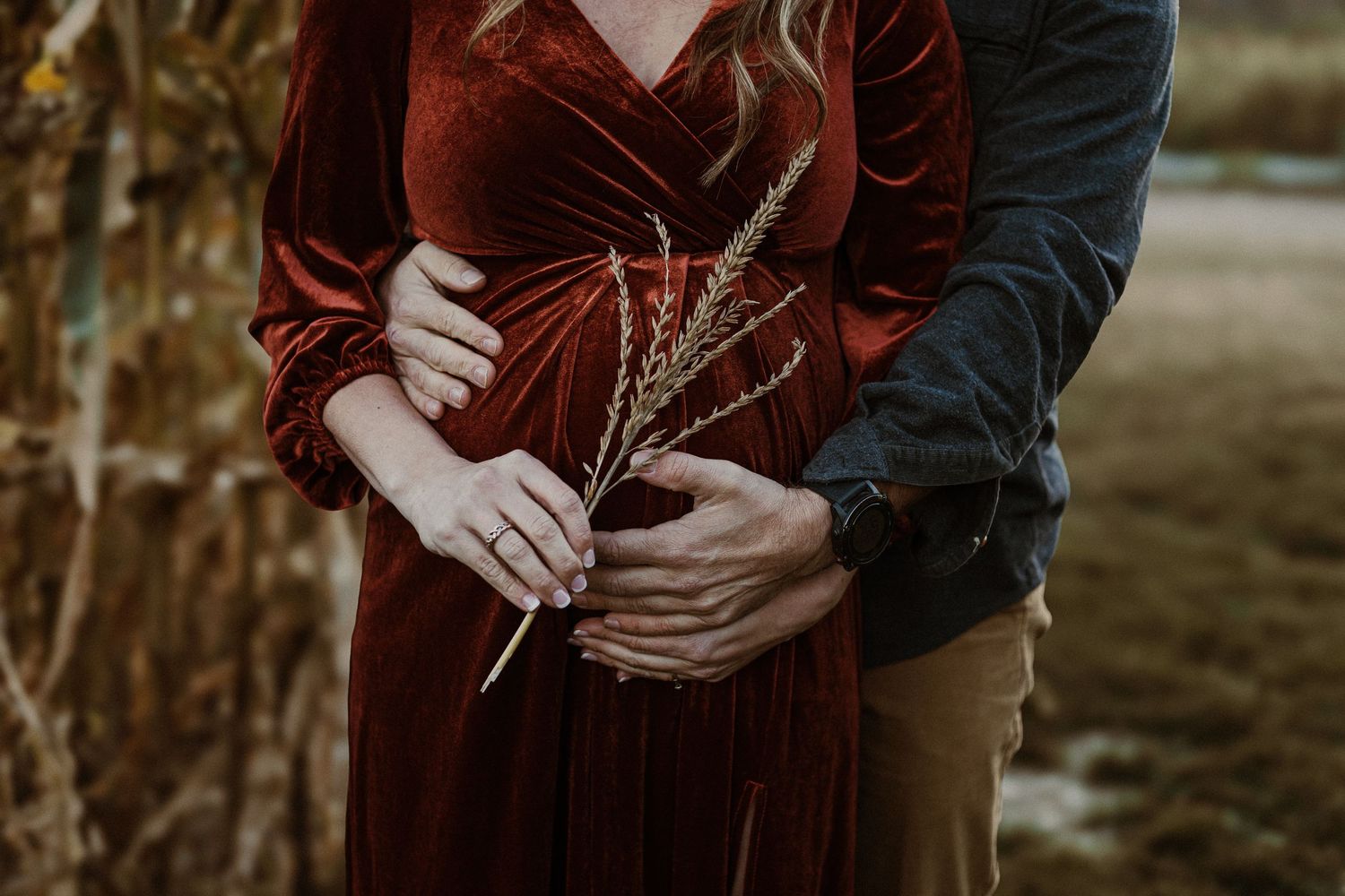 Couple embraces while holding dried flowers, woman wearing burgundy velvet dress.