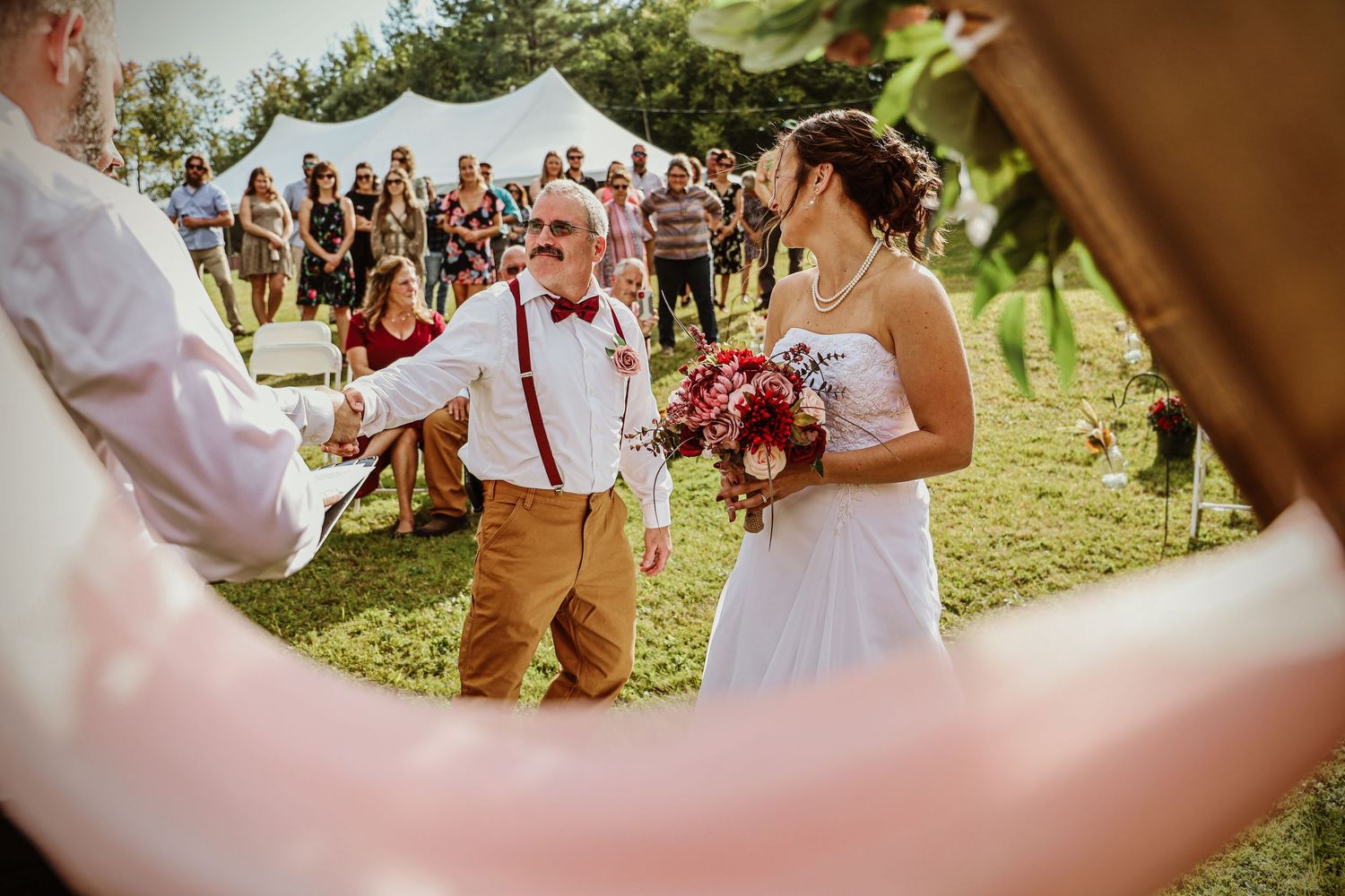 Wedding celebration on a sunny lawn with white tent and guests in background.
