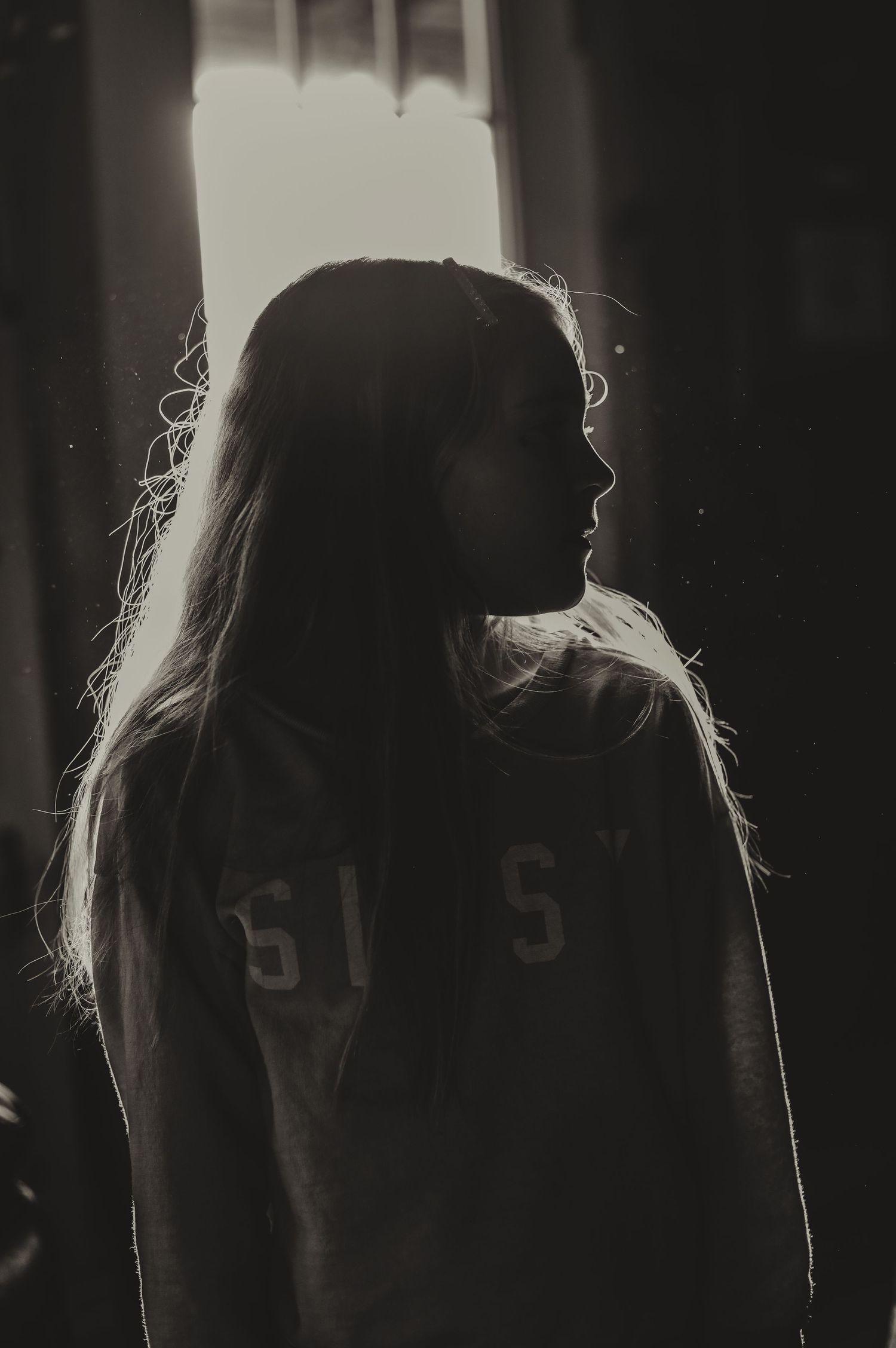 Silhouette of long-haired figure wearing a numbered sweatshirt against backlit window.