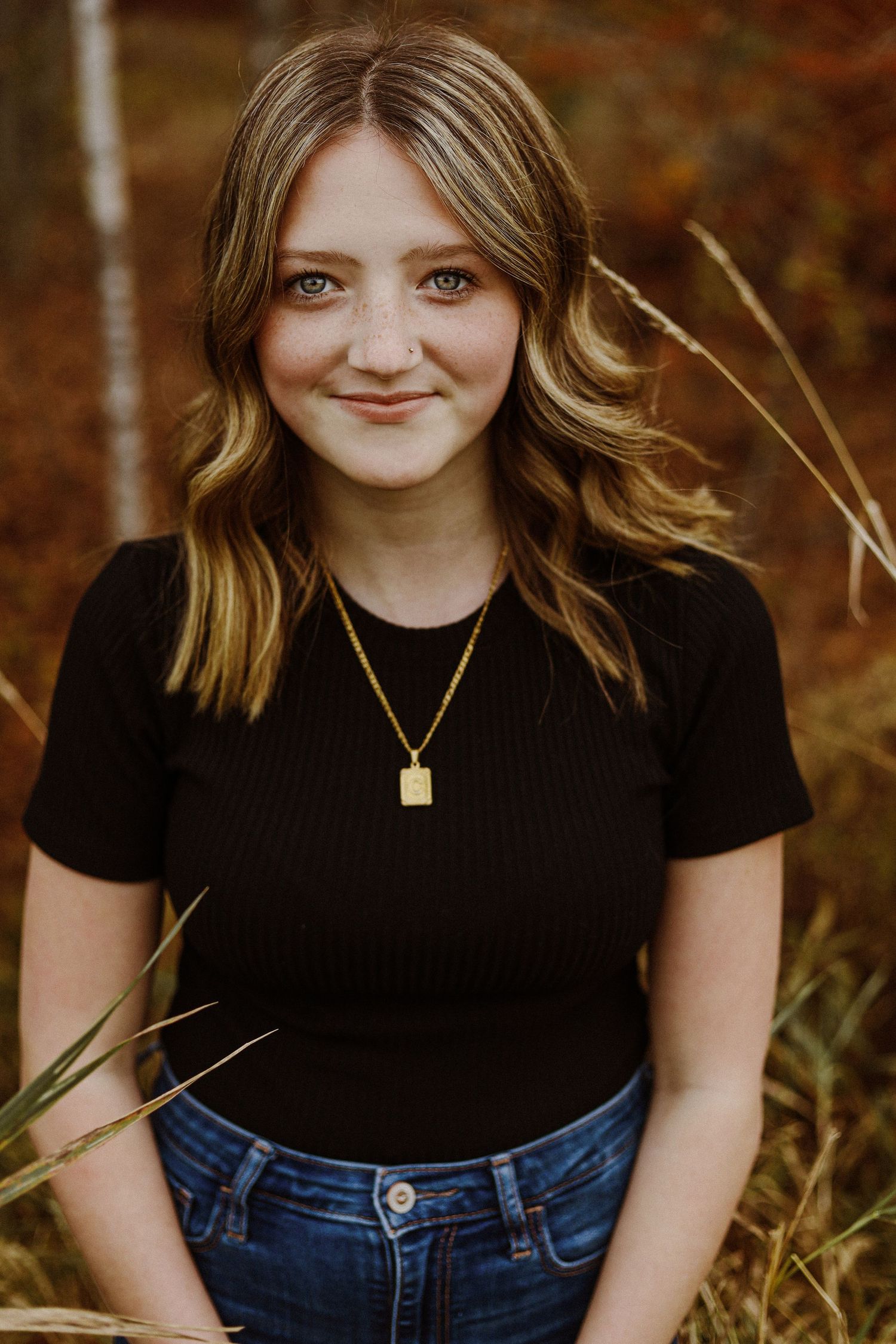 Portrait of a young woman in a black t-shirt and denim against an autumn background.