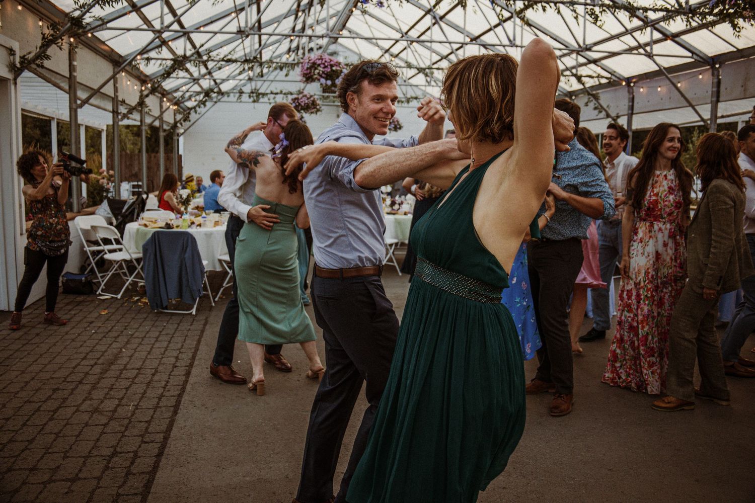 Wedding guests dancing and celebrating in a greenhouse-style venue.