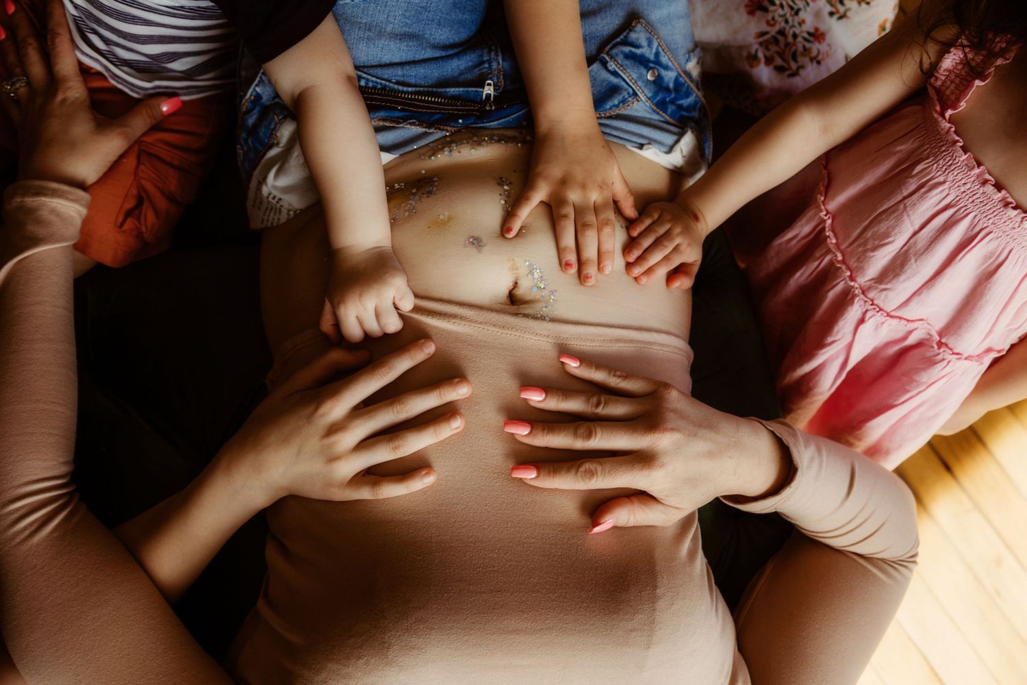 Multiple hands touching a pregnant belly in an intimate family moment.