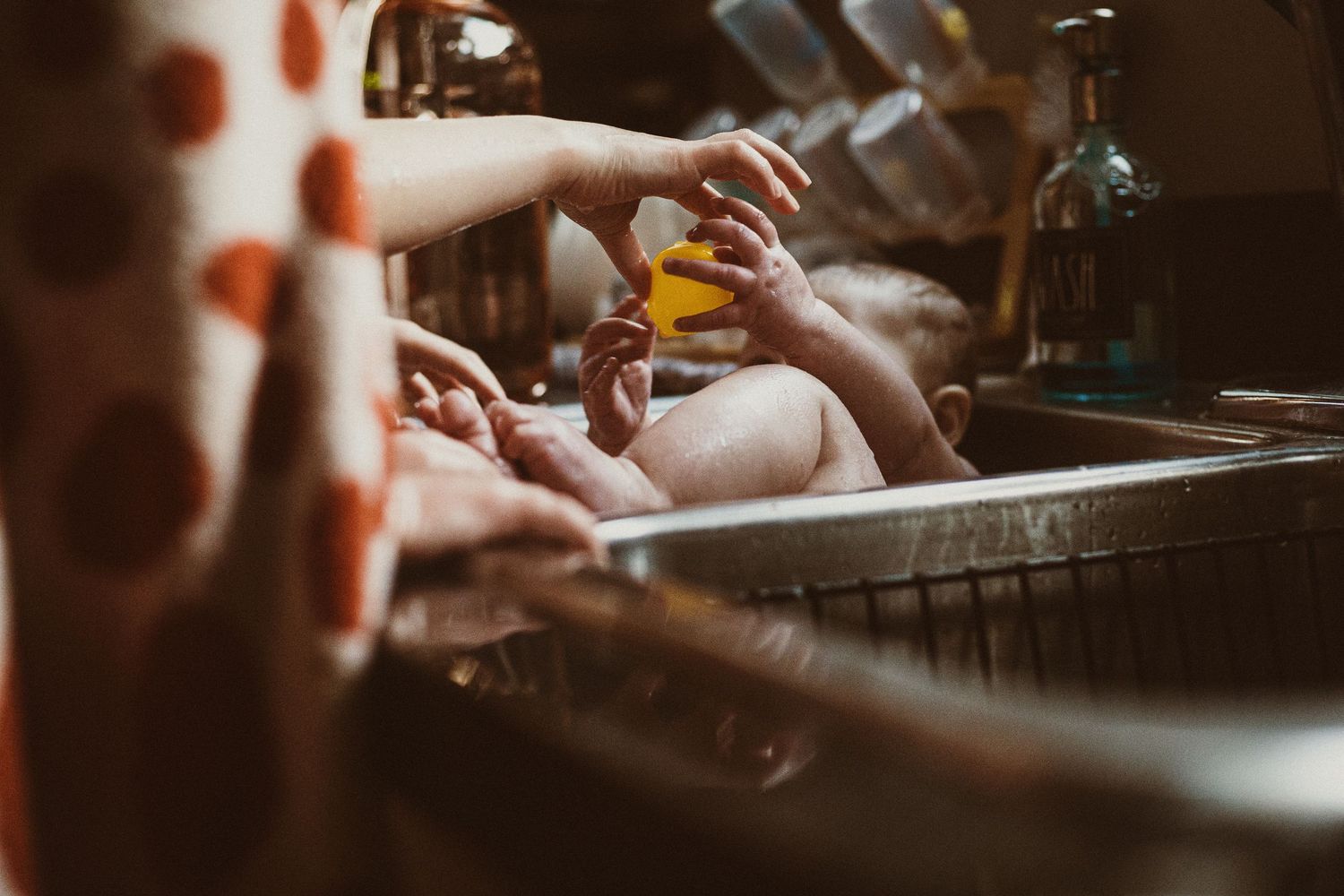 Two hands reaching for drinks at a dimly lit bar counter with glasses and bottles visible in the background.