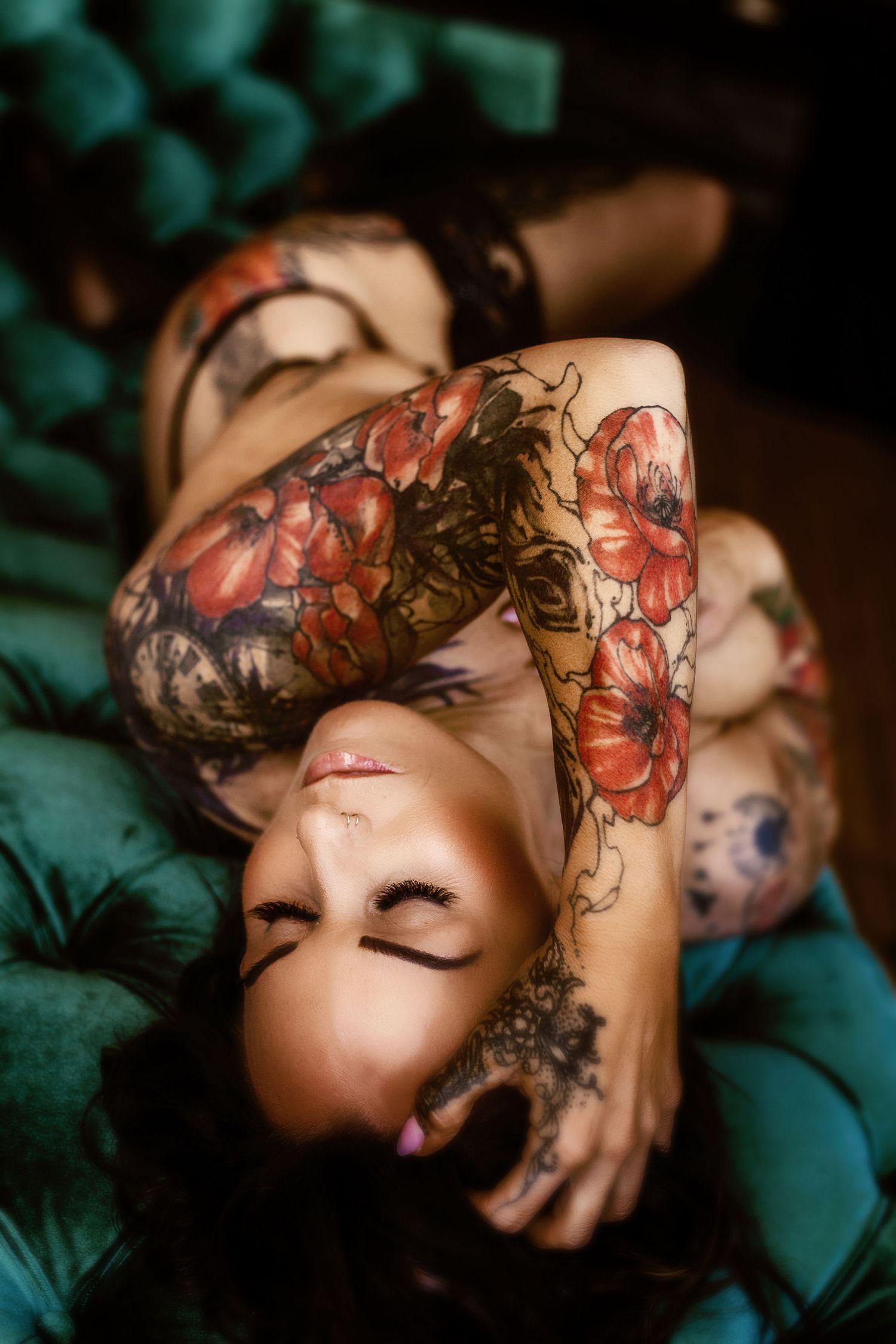 Artistic boudoir photo showing bright floral tattoos against dark teal tufted velvet fabric.