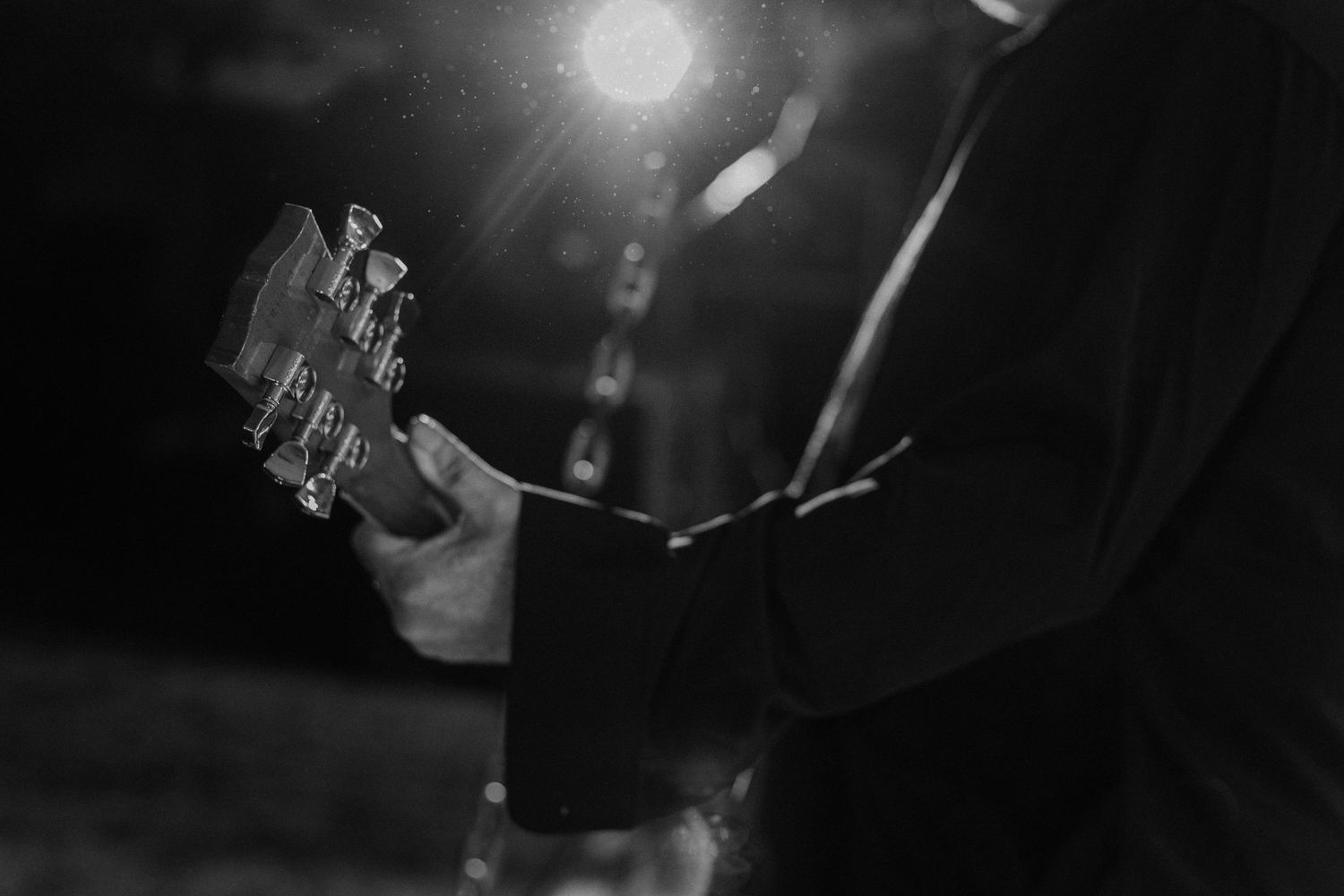 Black and white close-up of hands playing acoustic guitar in dim lighting.
