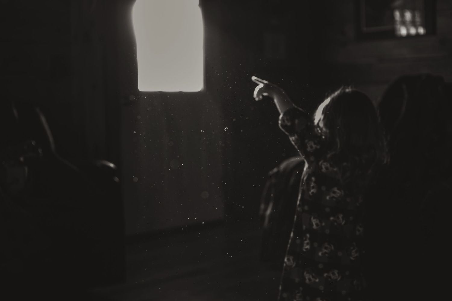 Silhouetted figure pointing upward in a dark room with window light.