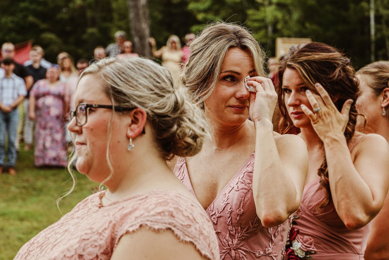Wedding party members in pink dresses share an emotional moment.