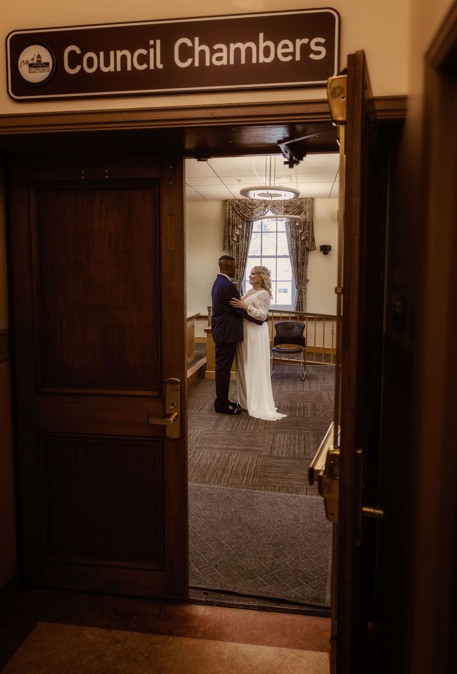 Wedding ceremony in council chambers viewed through wooden doorway entrance.