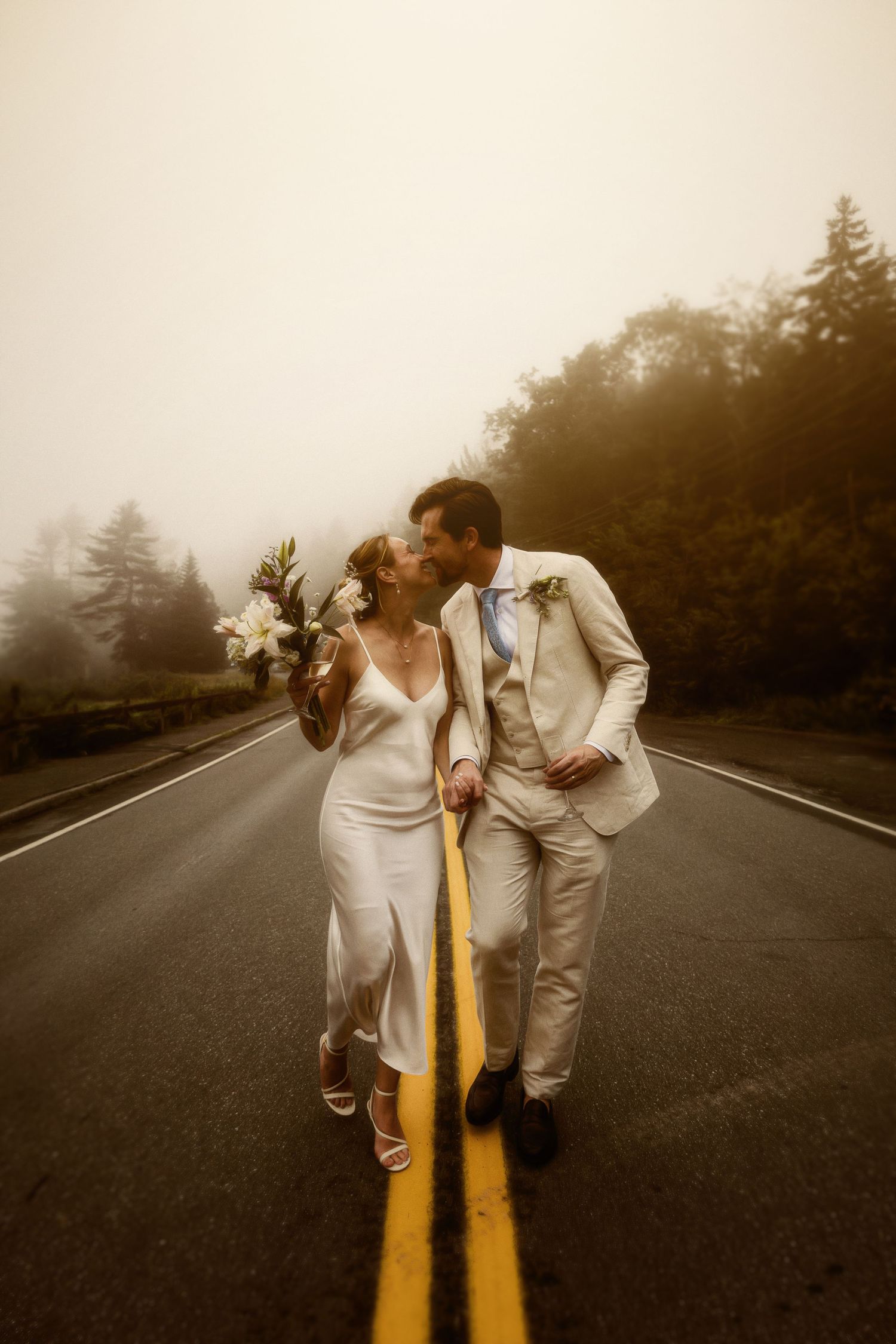 Wedding couple sharing a kiss on a misty road with yellow lines.