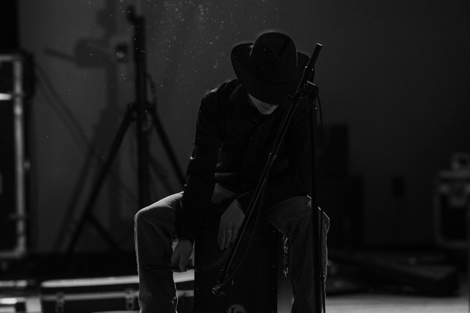 Silhouette of a musician sitting with instrument in dark studio setting.