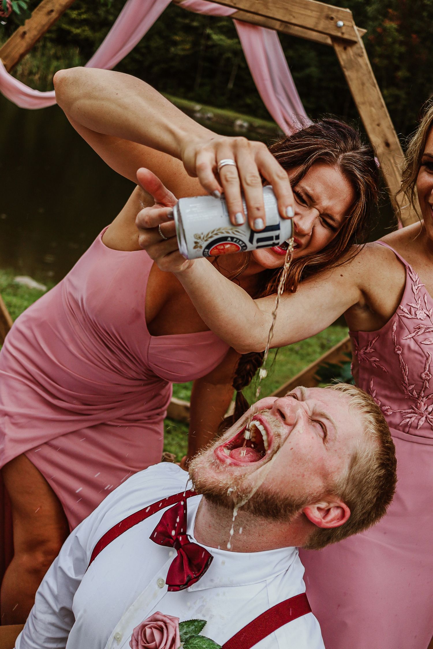 Playful moment as drink is poured at wedding celebration under wooden arch.