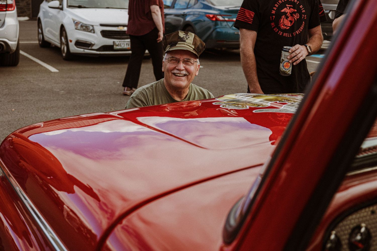 Someone smiling while looking through the window of a shiny red classic car.