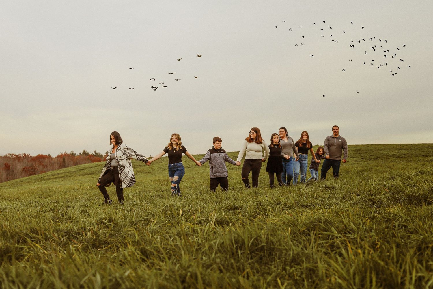 Group running through a grassy field with birds flying overhead in moody lighting.