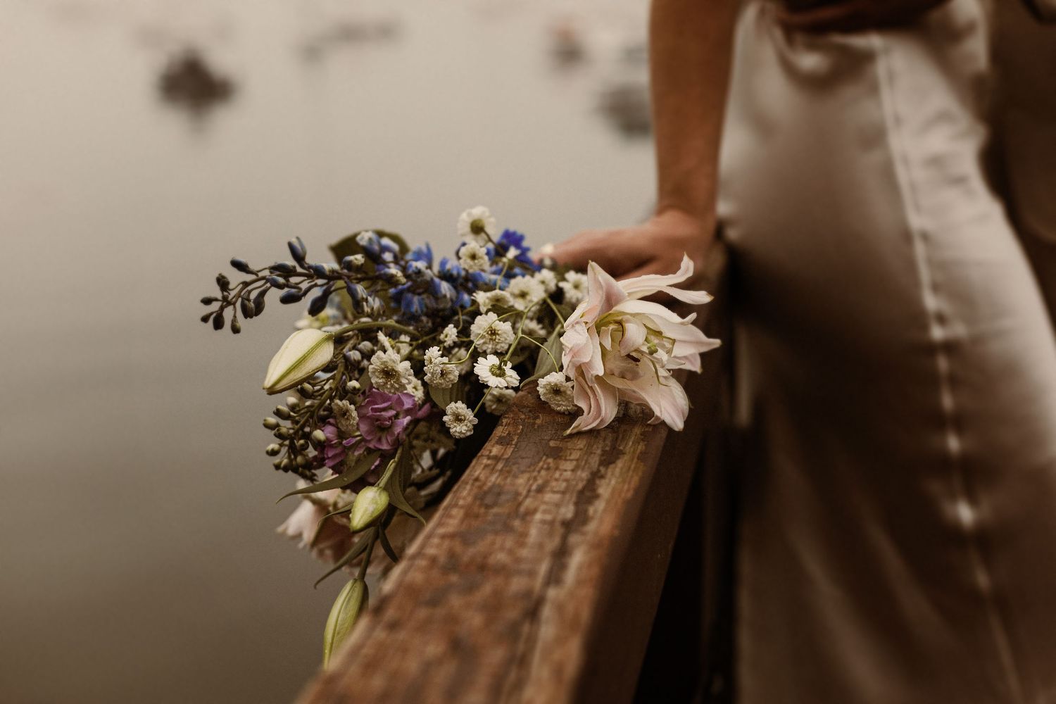 Delicate wildflower bouquet with white and purple blooms placed on rustic wooden railing.