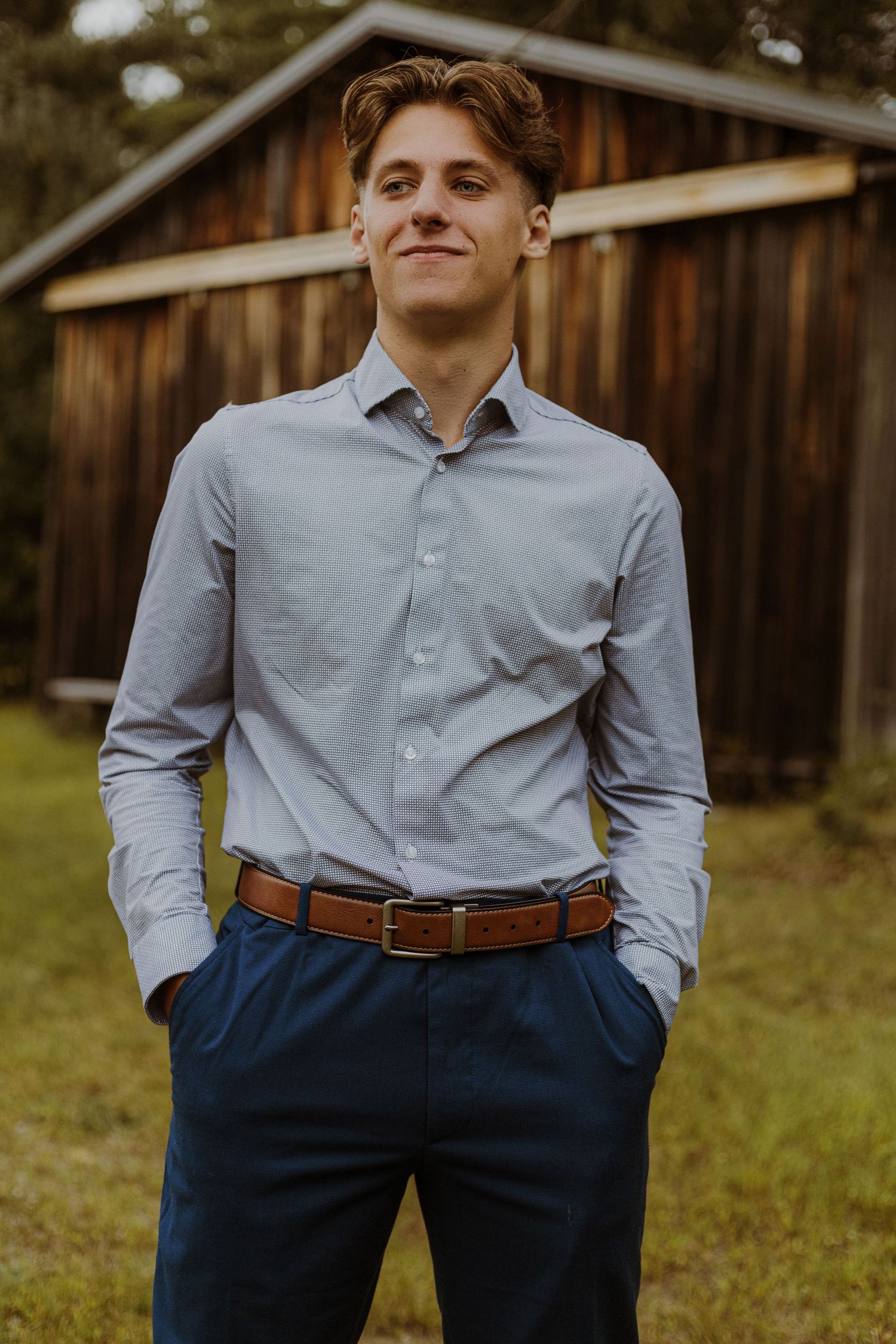 Professional portrait of a person in business attire standing in front of a wooden structure.