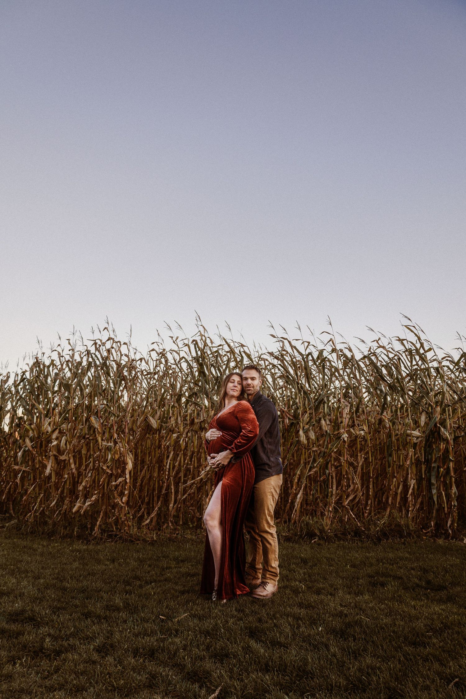 Couple in romantic embrace standing beside tall cornfield at sunset.