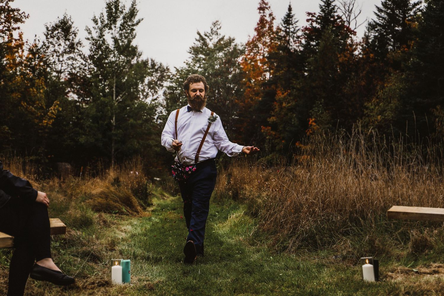 Wedding photographer with suspenders walks through autumn field setting.