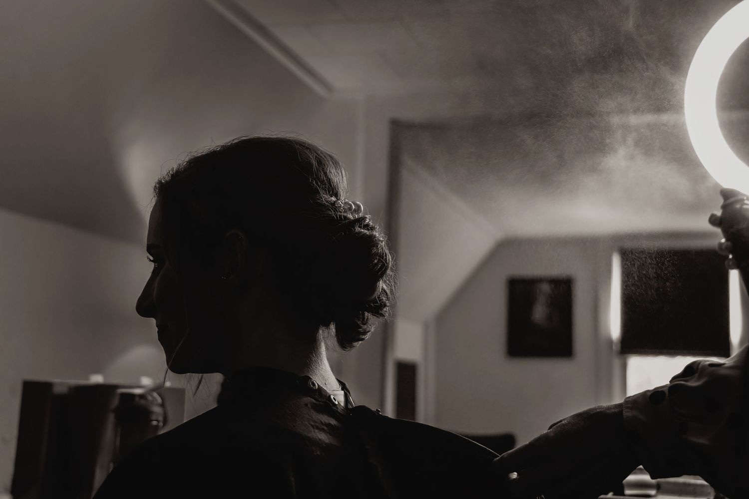 Artistic black and white silhouette of wedding preparation in indoor lighting.