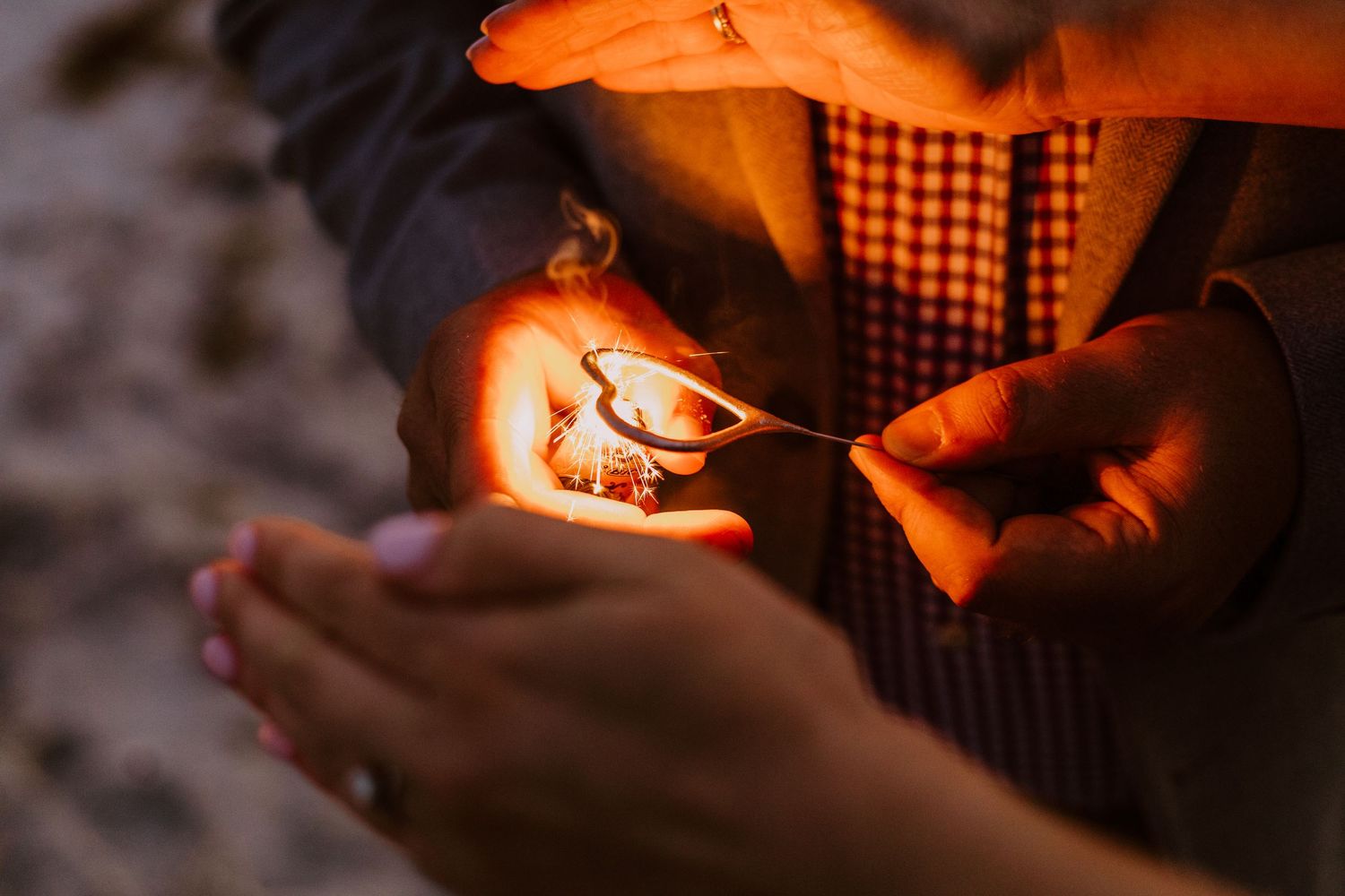 Hands cupped around a glowing sparkler creating warm orange light in the darkness.