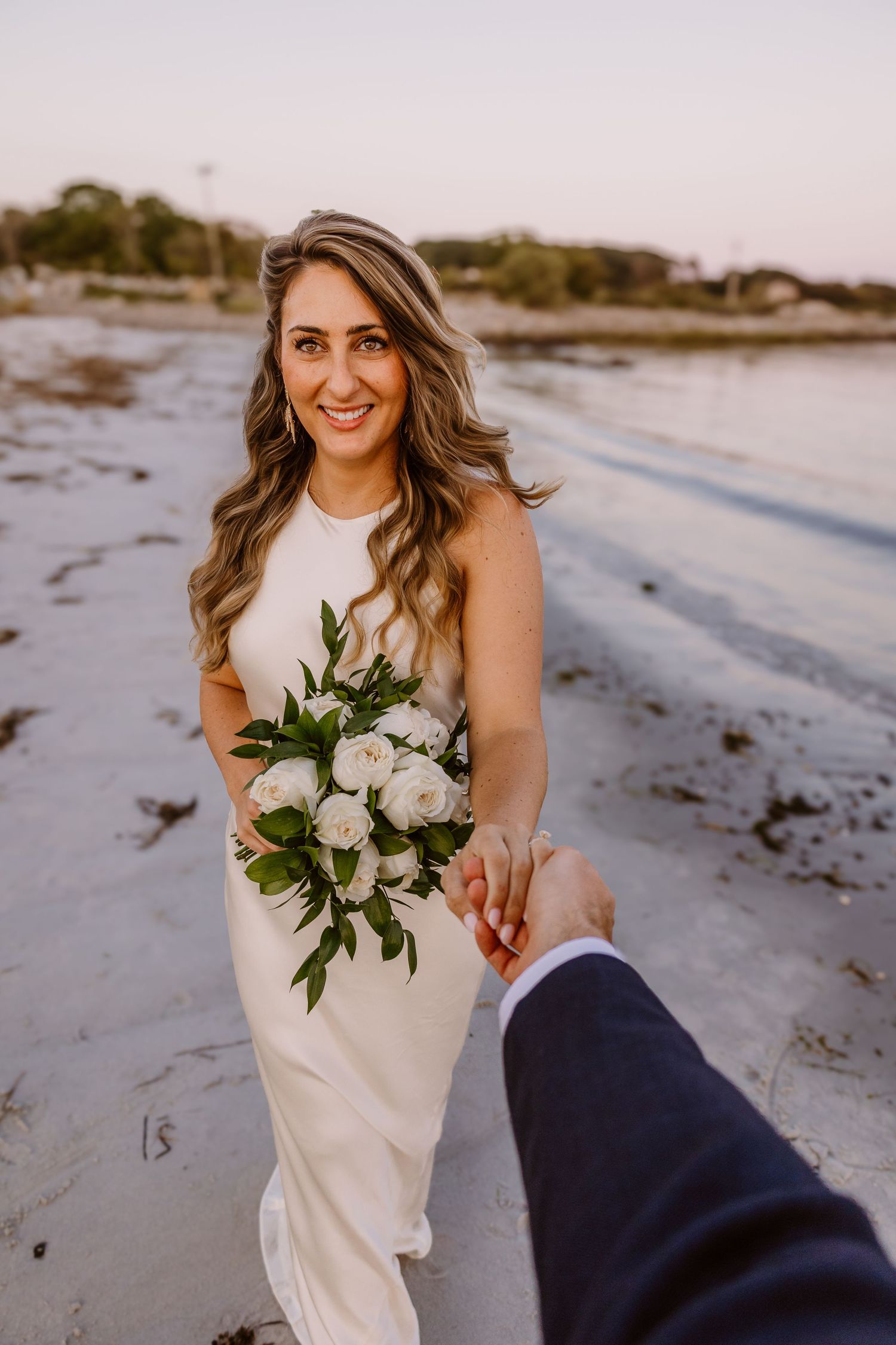 A beachside bridal portrait featuring a white dress and natural bouquet.